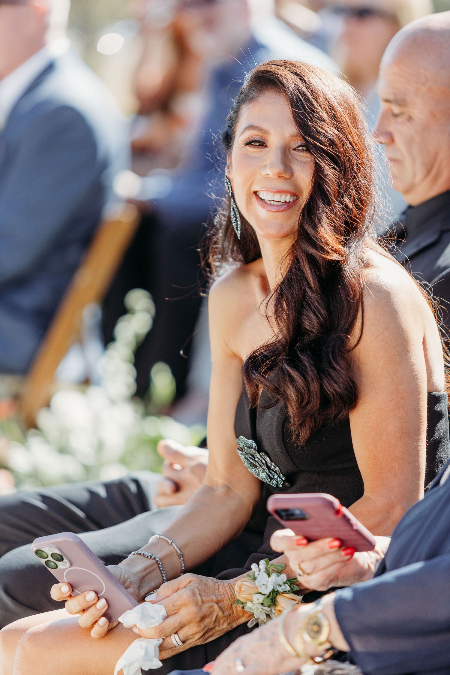 Wedding guests share laughter and conversation while seated at an outdoor reception during a sunny afternoon.