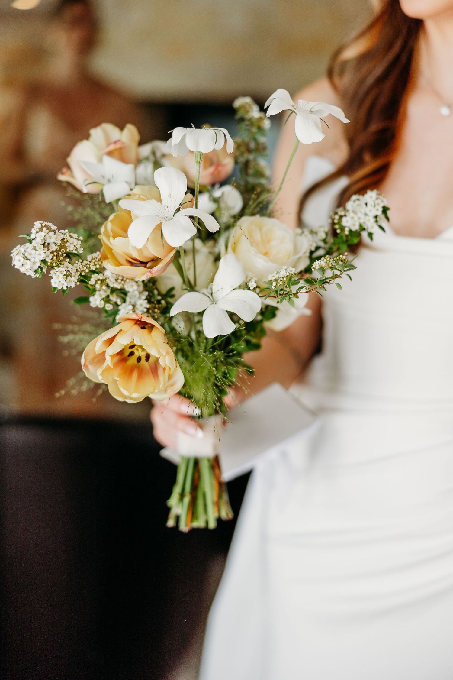 Close-up view of a delicate bridal bouquet with white and peach flowers against a white wedding dress.