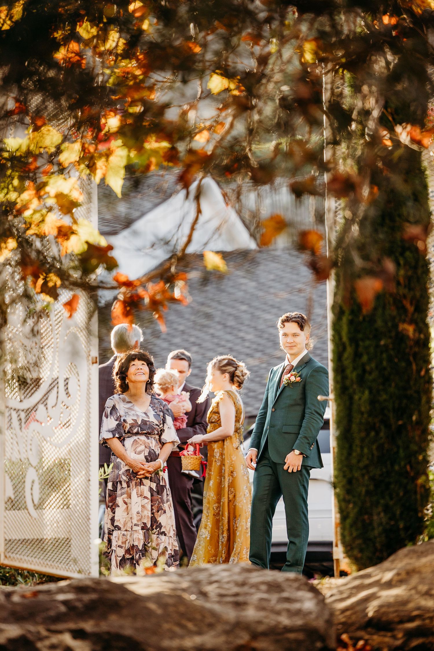 Wedding party gathered under autumn trees with golden leaves during outdoor celebration.