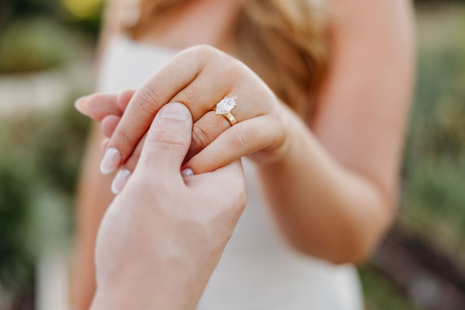 Close-up of hands showing off a sparkling engagement ring in natural outdoor lighting.