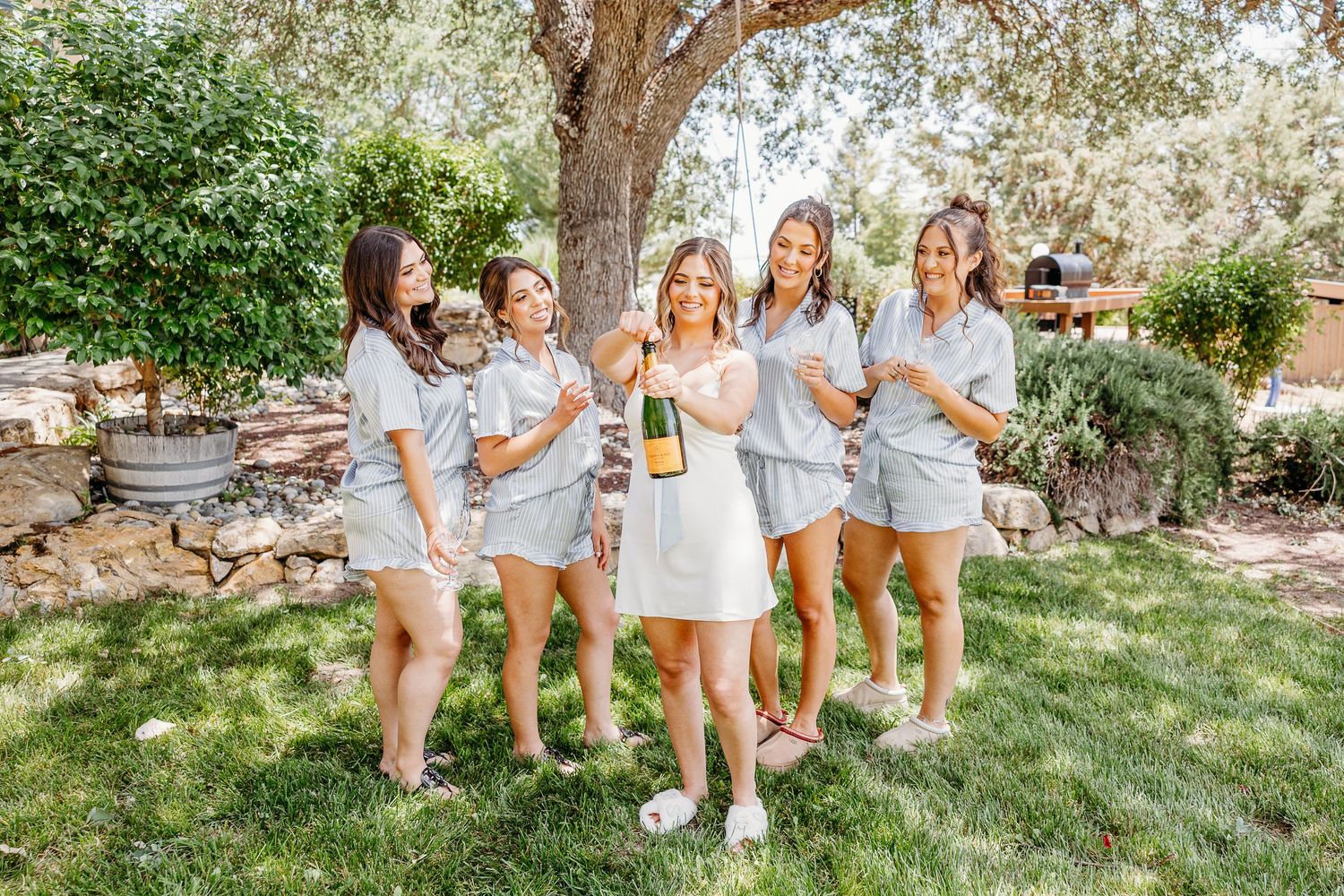Friends in matching outfits enjoy a casual outdoor gathering on a grassy lawn with trees in the background.