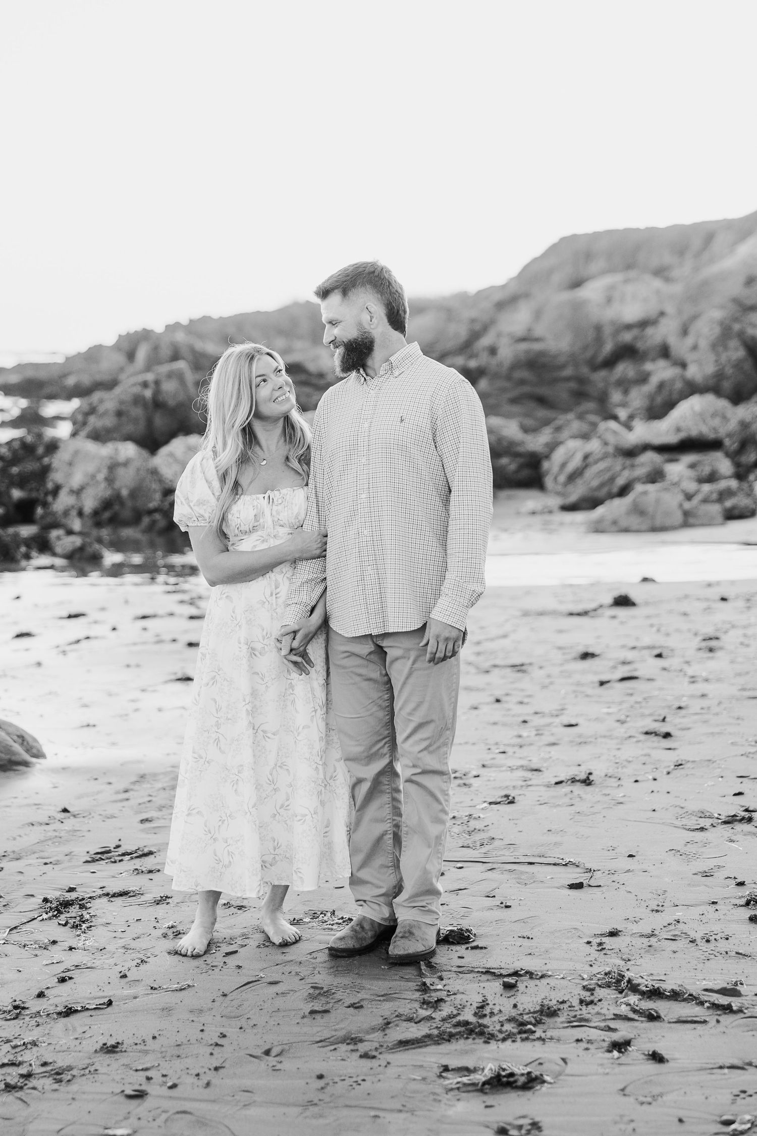 Black and white photo of romantic beach engagement session along rocky coastline.