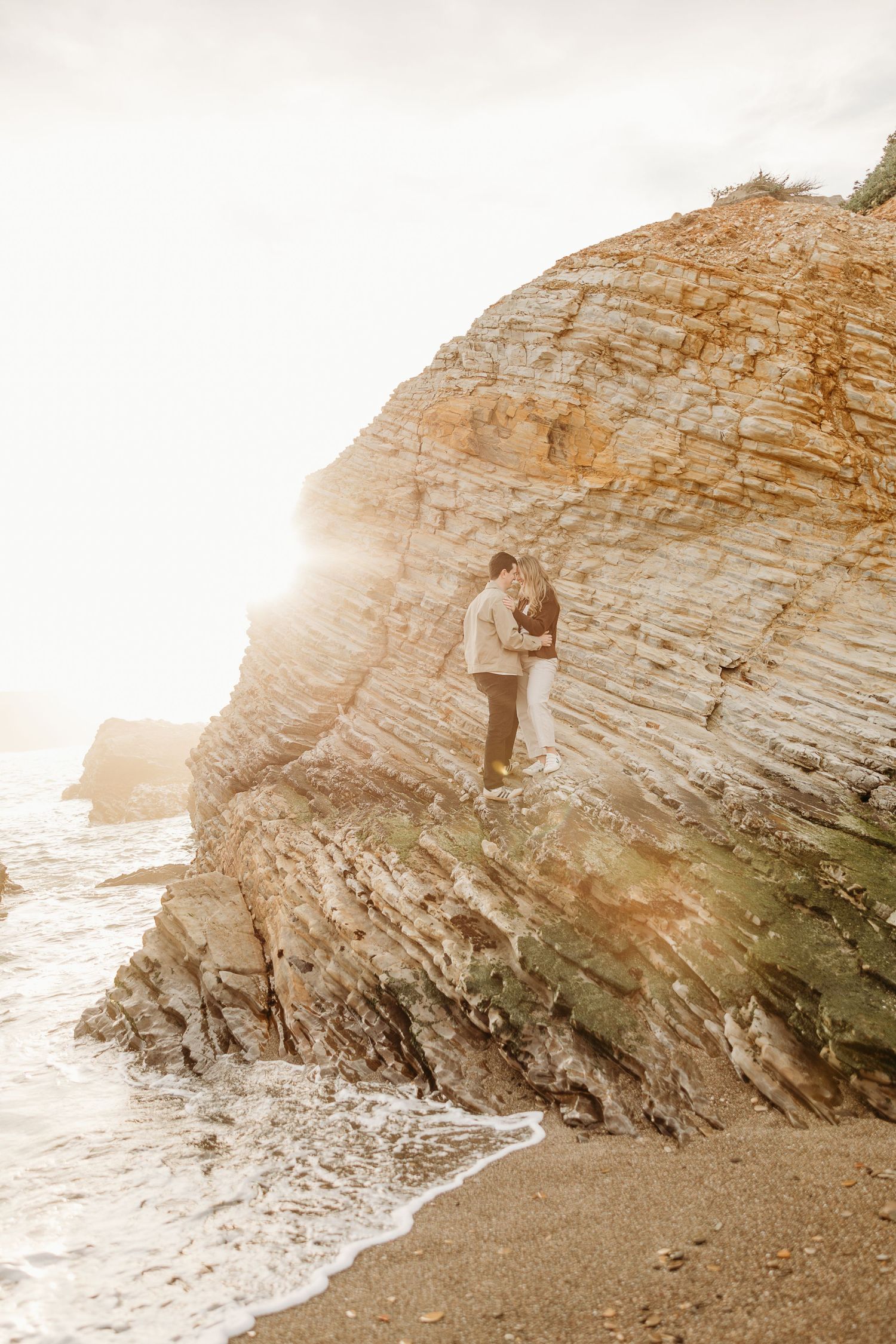 Dramatic coastal cliffs and rock formations at sunset create romantic backdrop for engagement photos.