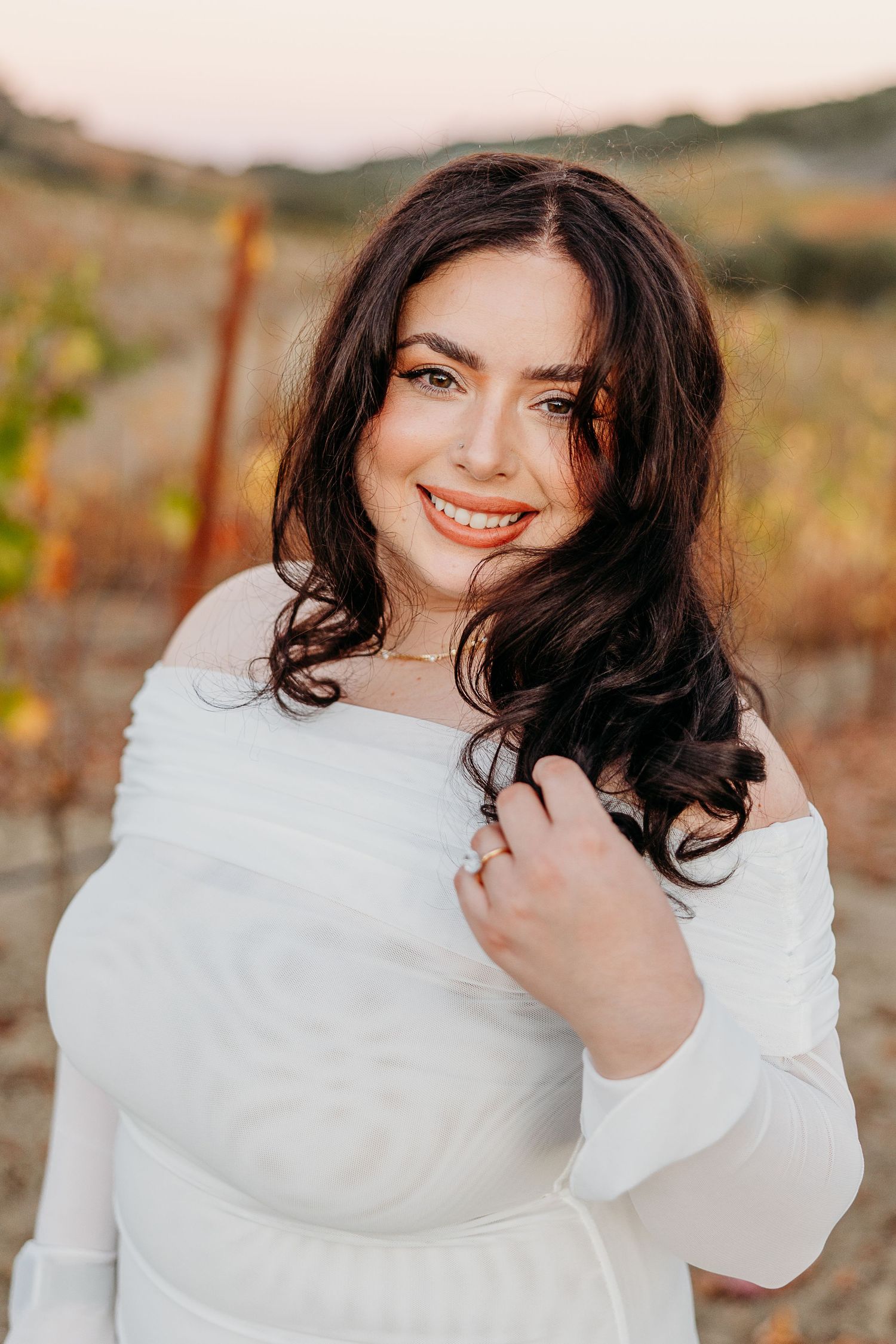 Woman in white sweater poses against autumn vineyard backdrop during golden hour.