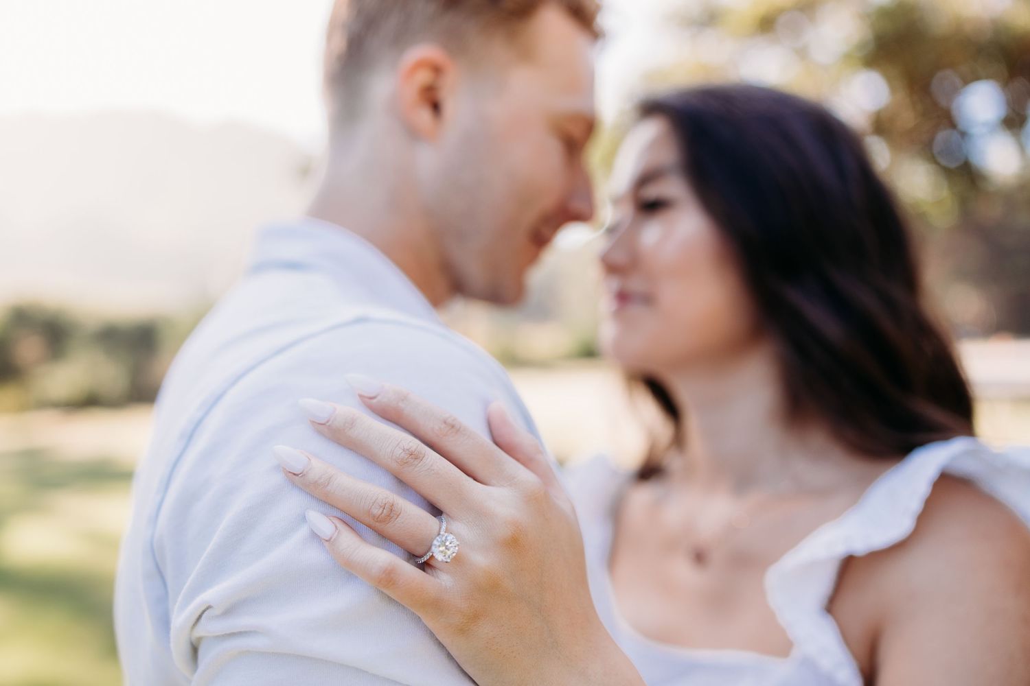 Close up of engaged couple showing off diamond ring in outdoor setting.