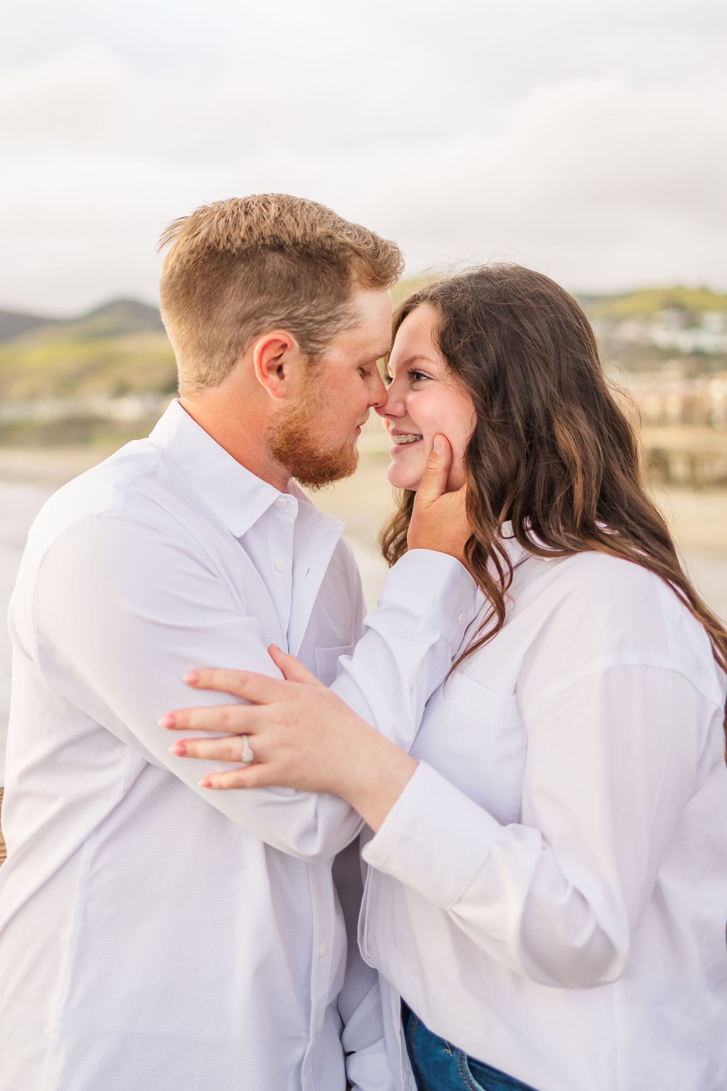 A loving couple in white shirts sharing an affectionate moment on a oceanside boardwalk.
