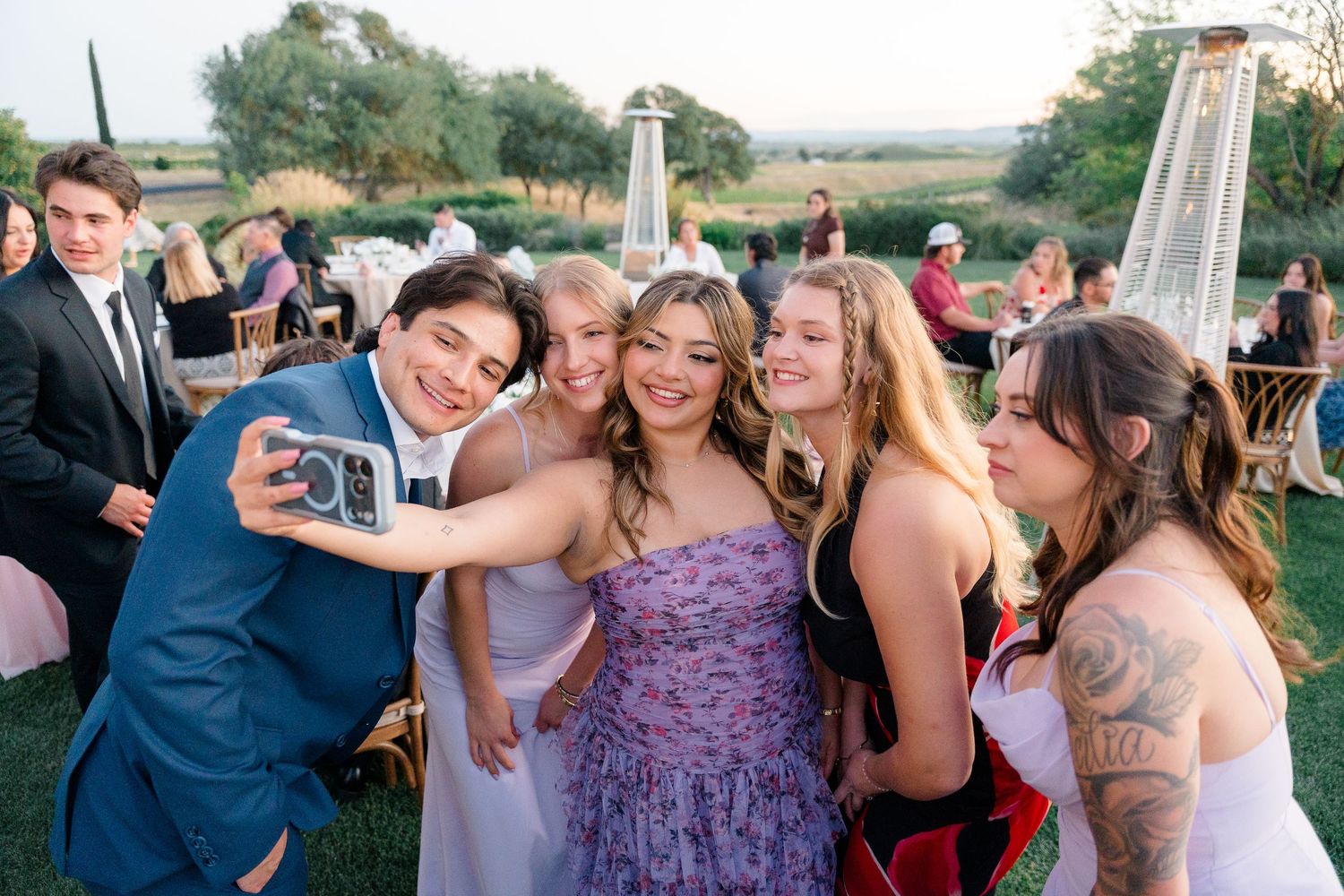 Wedding guests taking a group selfie with instant camera at outdoor vineyard reception.