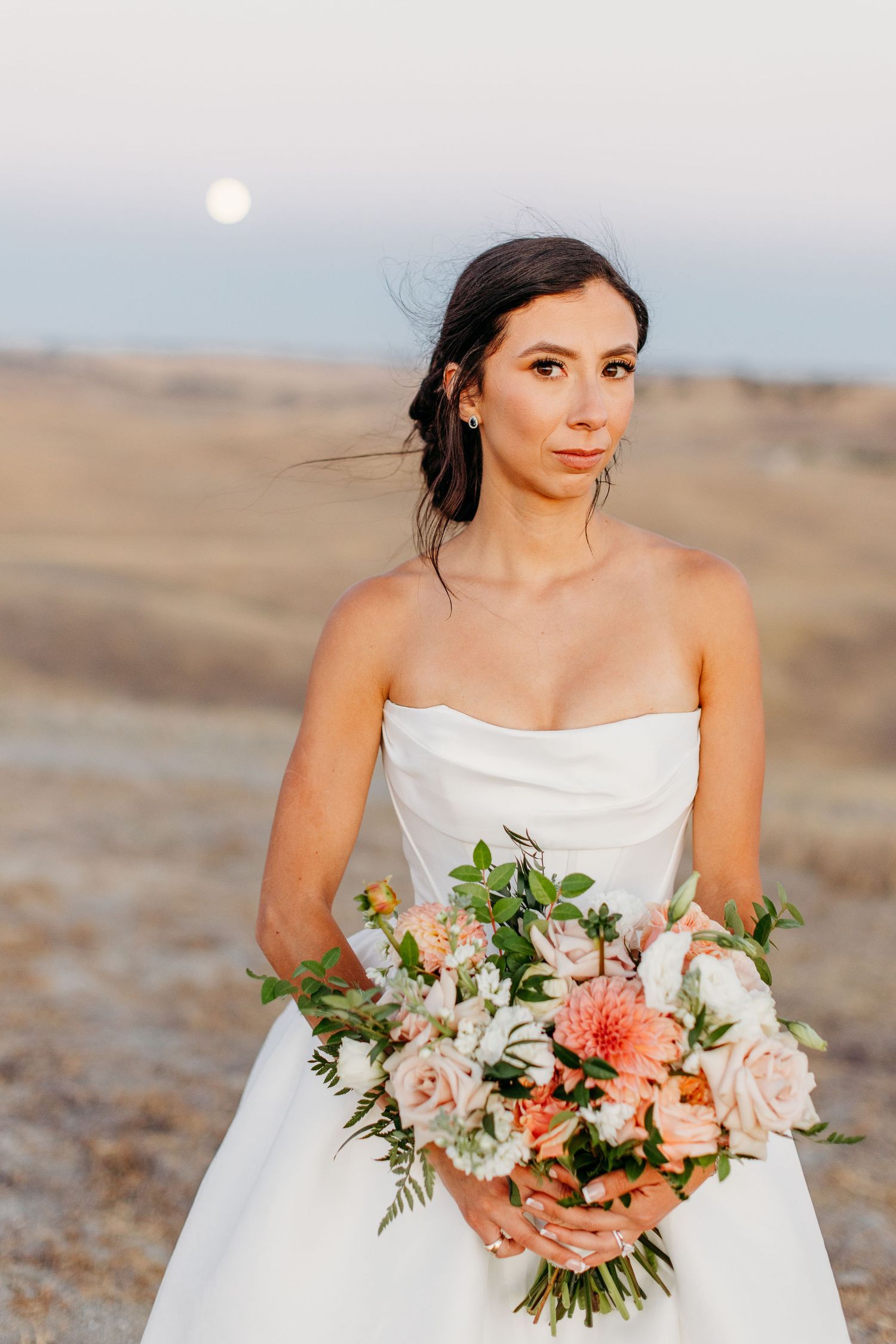 Elegant bridal portraits with peach floral bouquet against desert landscape at sunset.