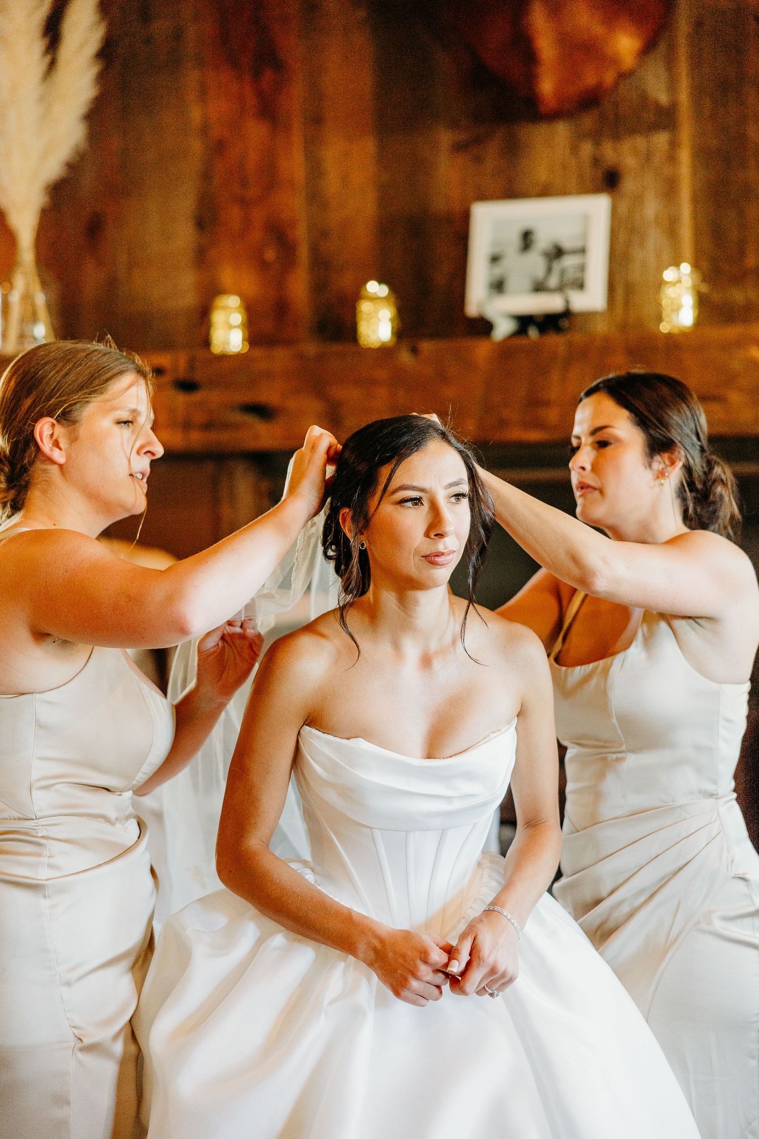 A row of bridesmaids in white dresses stand together in a rustic barn setting.