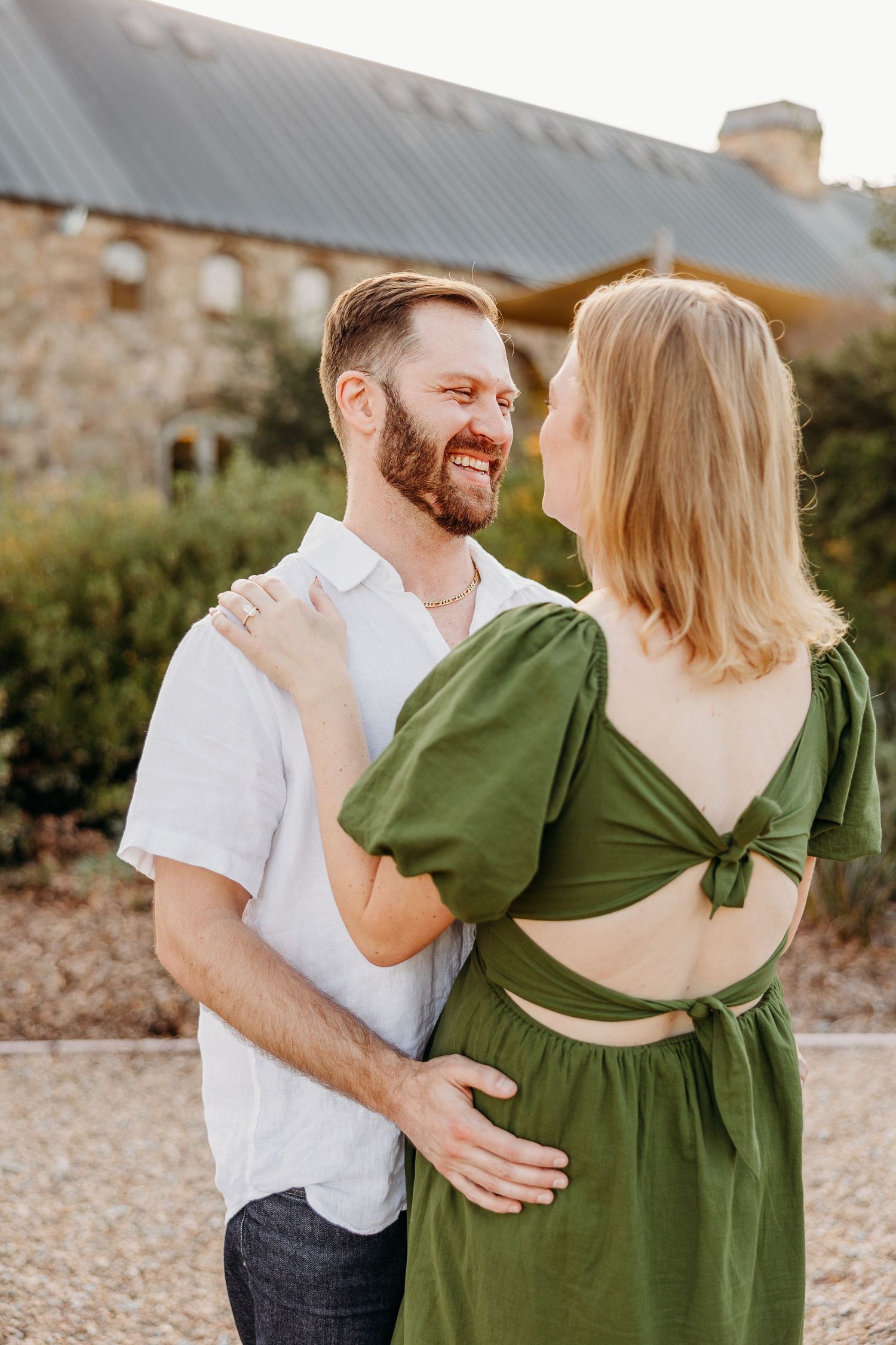 A couple shares a tender moment outdoors, with the person in green leaning back against their partner in white.