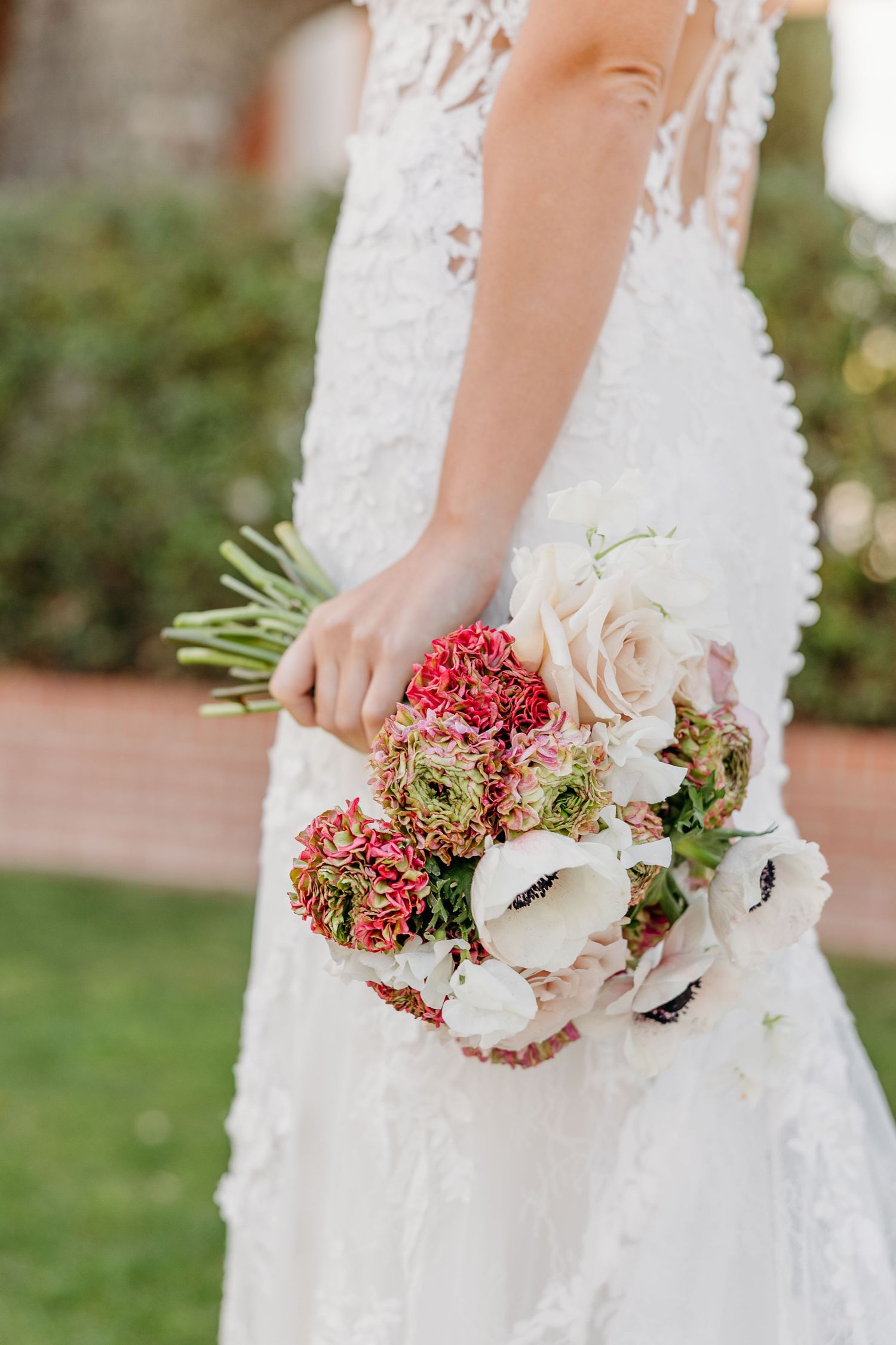 Close-up view of a bridal bouquet featuring white anemones and red berries against a lace wedding dress.