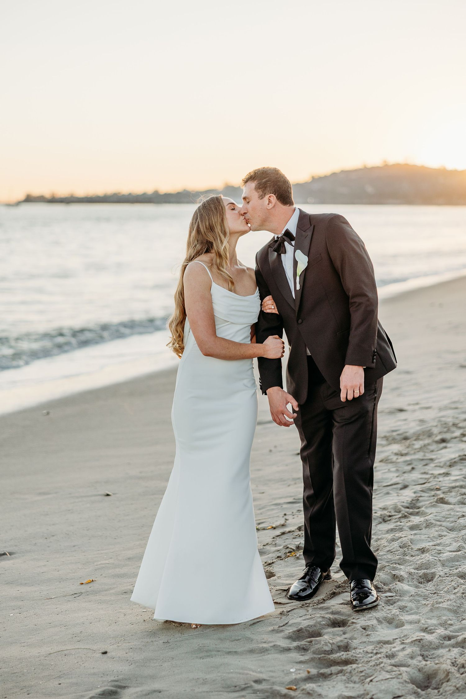 Romantic beach wedding photos at sunset with waves in the background.
