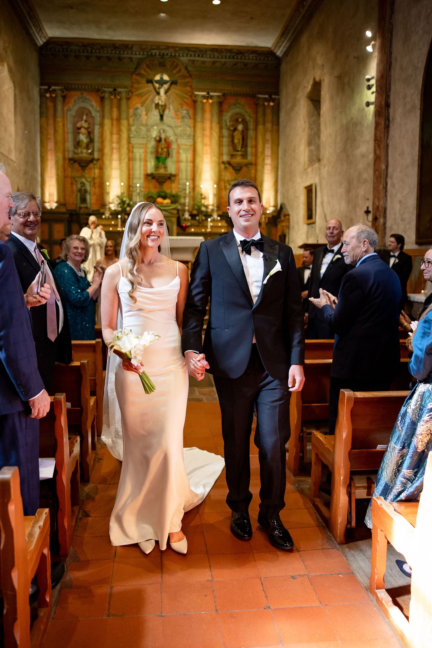 Wedding ceremony guests mingle in the pews of an ornate church with decorative altars and religious artwork.