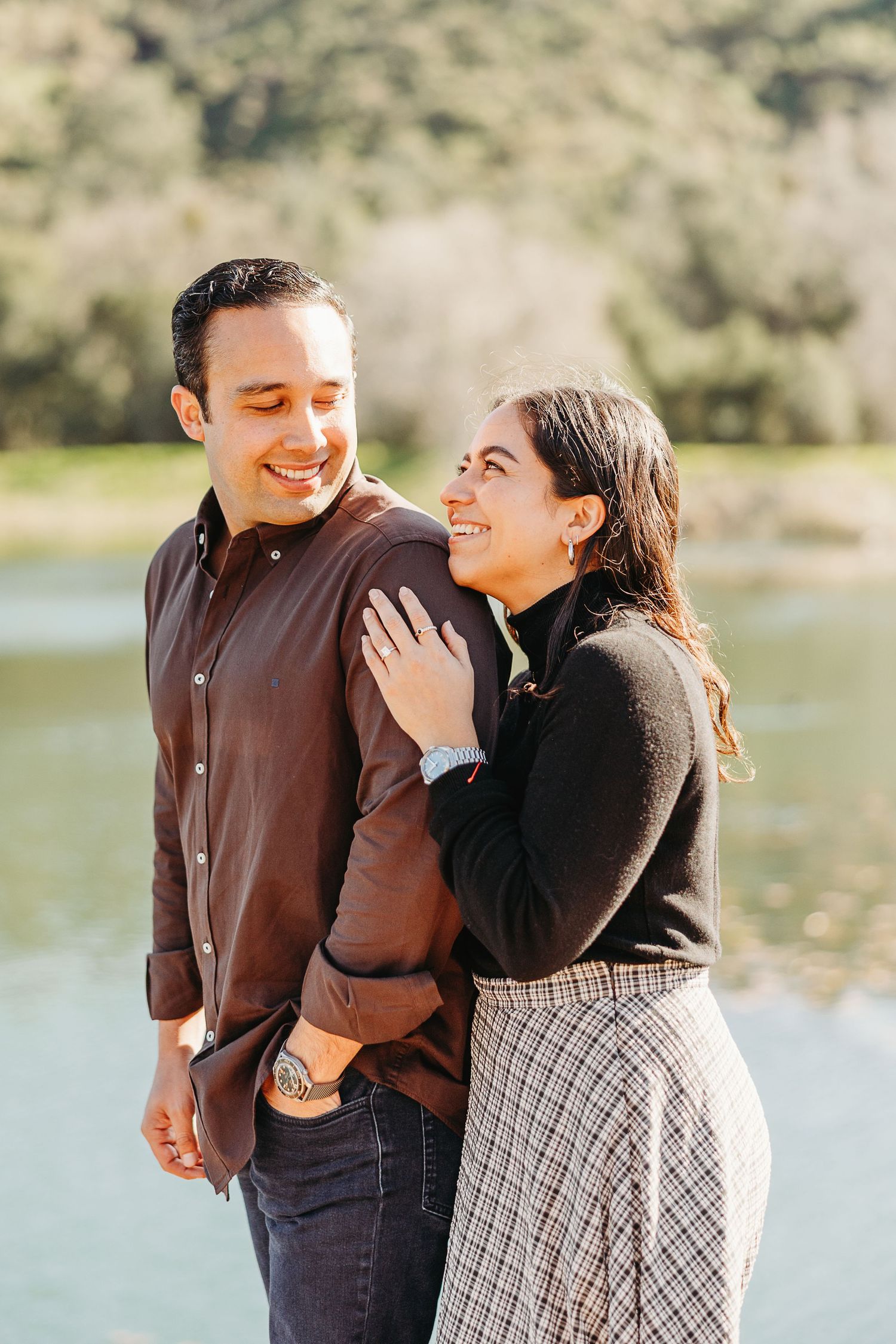 Couple sharing joyful moments and laughter by a serene lake on a sunny afternoon.