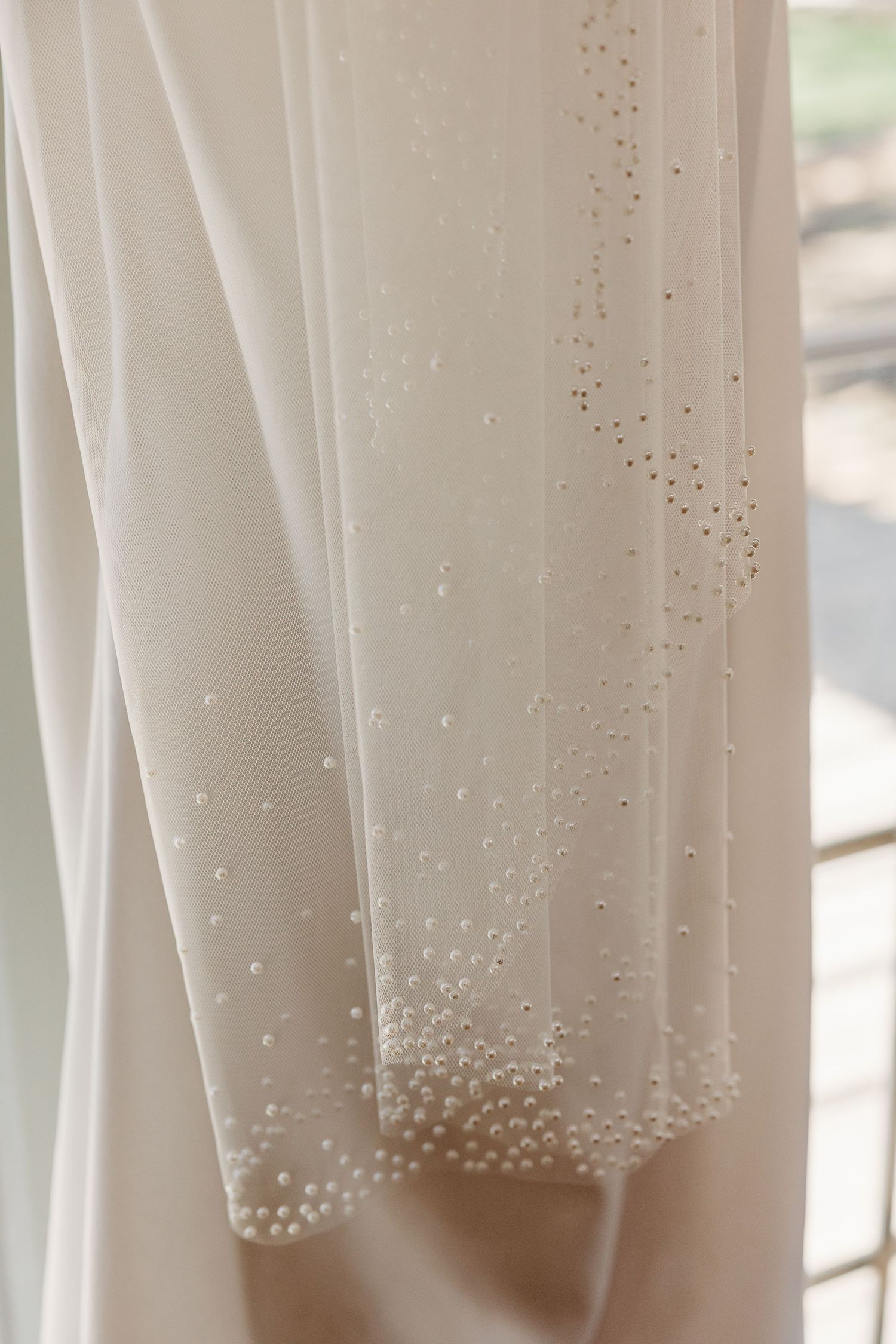 Delicate beaded details adorn the hem of a white wedding dress veil against a light background.