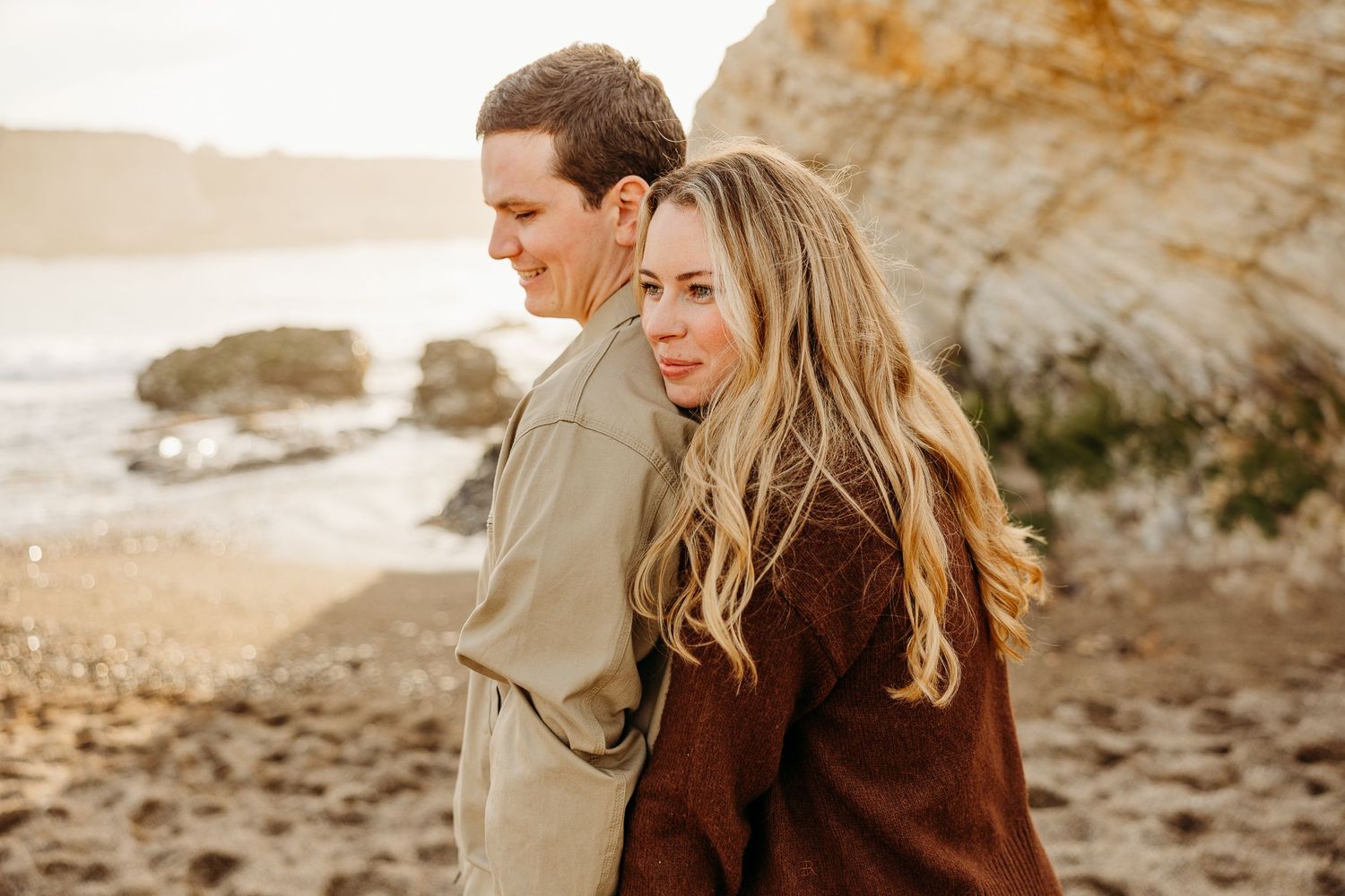A romantic couple embraces outside a rustic doorway with stone walls and wine barrel decoration.