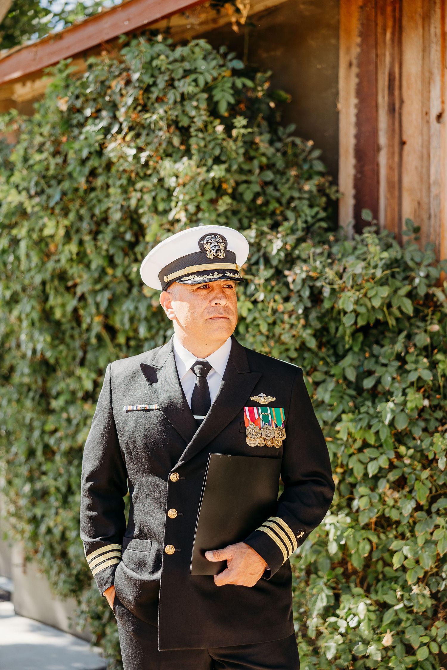 Military officers in formal dress uniforms standing at attention outdoors against a backdrop of green foliage.