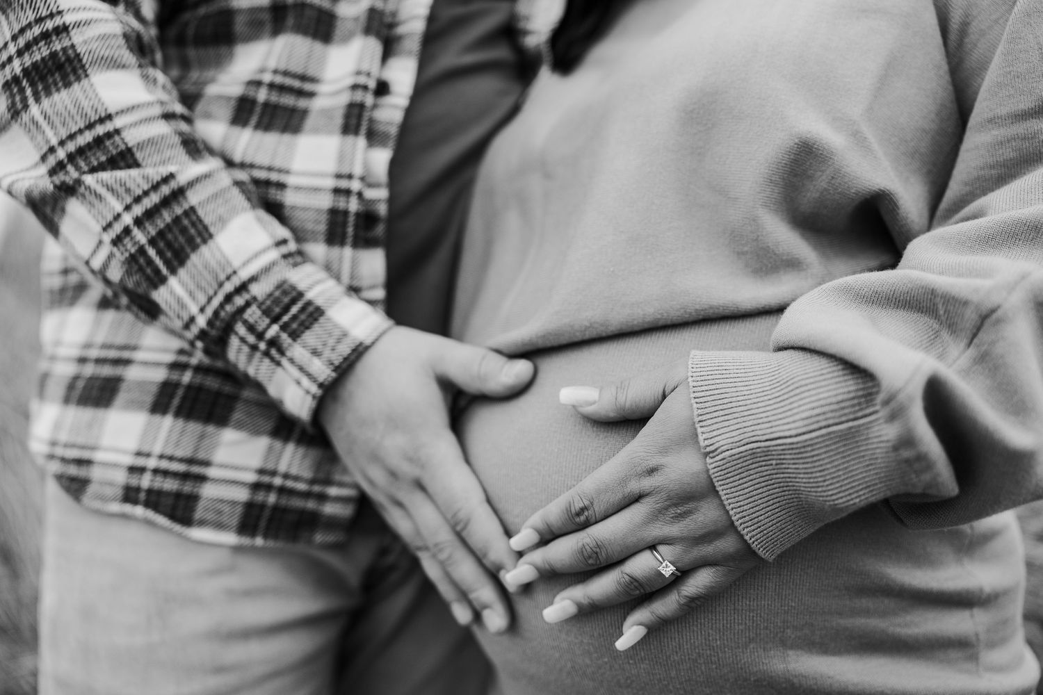 Close up black and white photo of hands forming a heart shape over a pregnant belly.