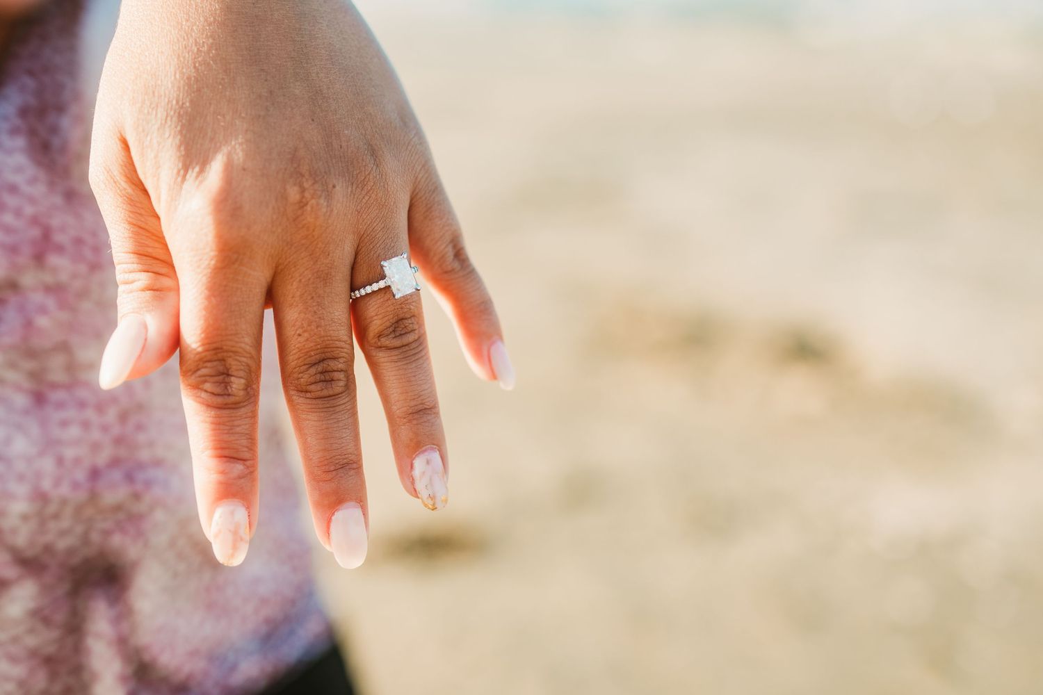 Close-up shot of hand displaying sparkling engagement ring against desert landscape.