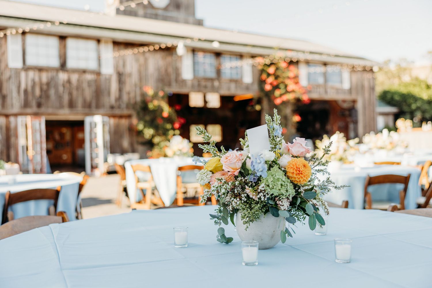 Rustic outdoor wedding reception table with peach and white floral centerpiece on light blue linen at Holland Ranch San Luis Obispo