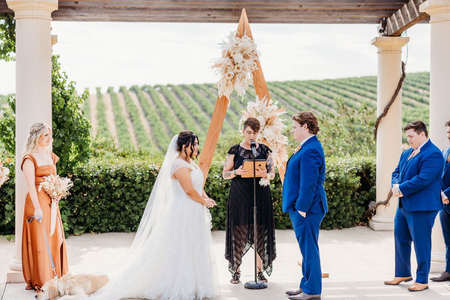 Wedding ceremony taking place under an elegant white pergola overlooking rolling vineyard hills.