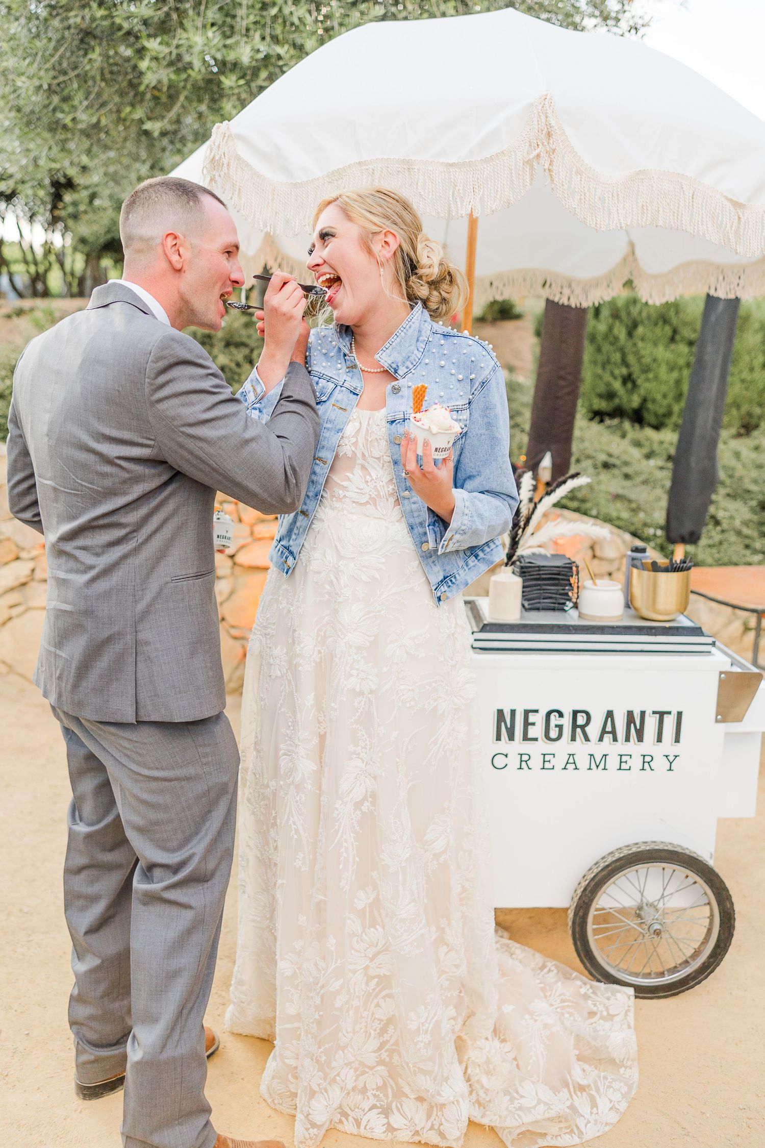 Newlyweds playfully feed each other ice cream at their outdoor wedding reception.