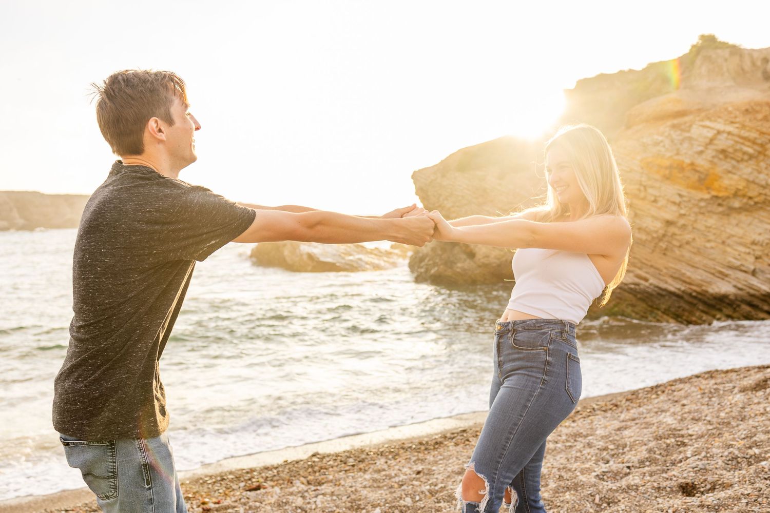 A playful couple dances together on a beach during sunset.