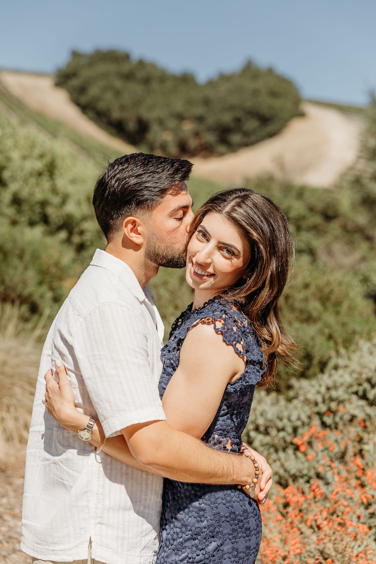 Couple sharing intimate moment among orange wildflowers in vineyard setting.