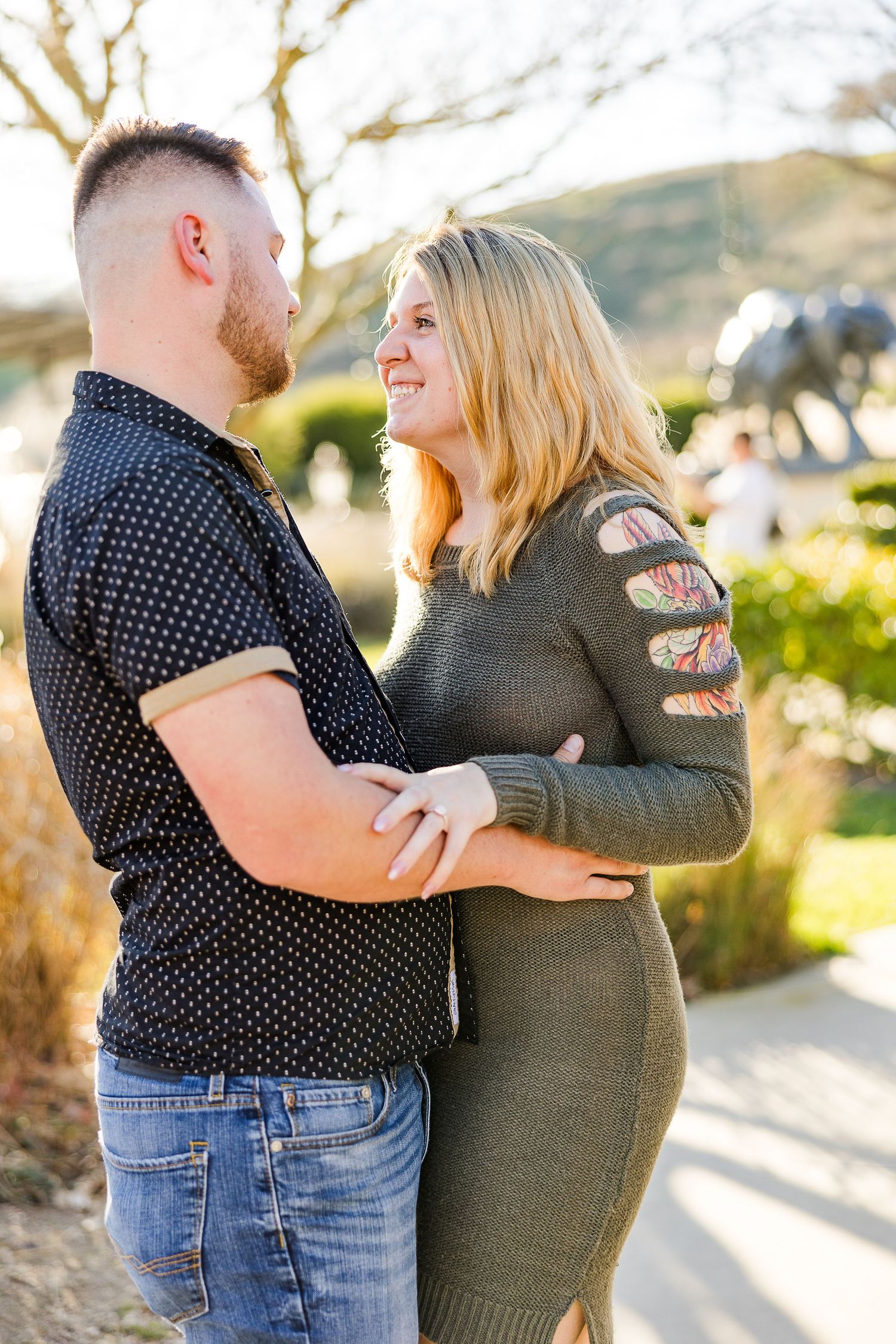 A couple in casual attire embraces on a sunlit garden path.