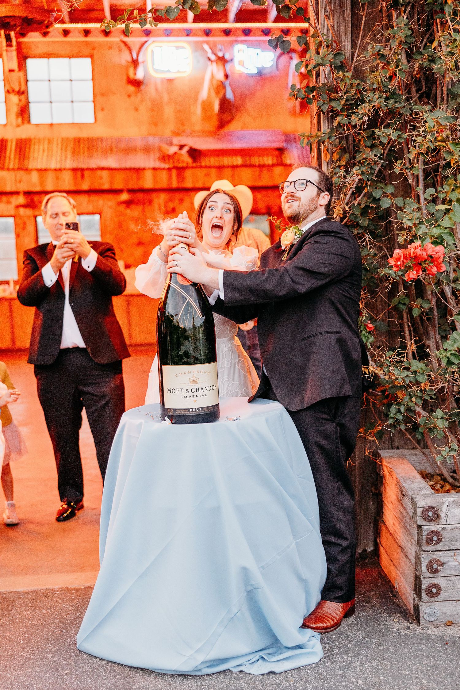 A celebratory moment with champagne being popped at a wedding reception with orange ambient lighting Holland Ranch SLO.