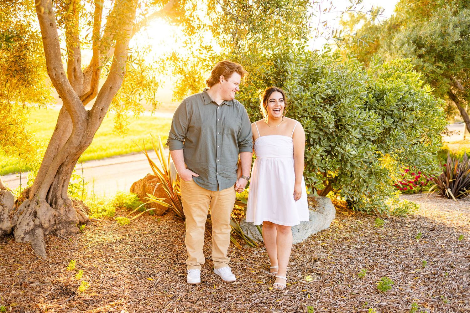 Couple takes romantic stroll through garden path with golden sunlight filtering through trees.