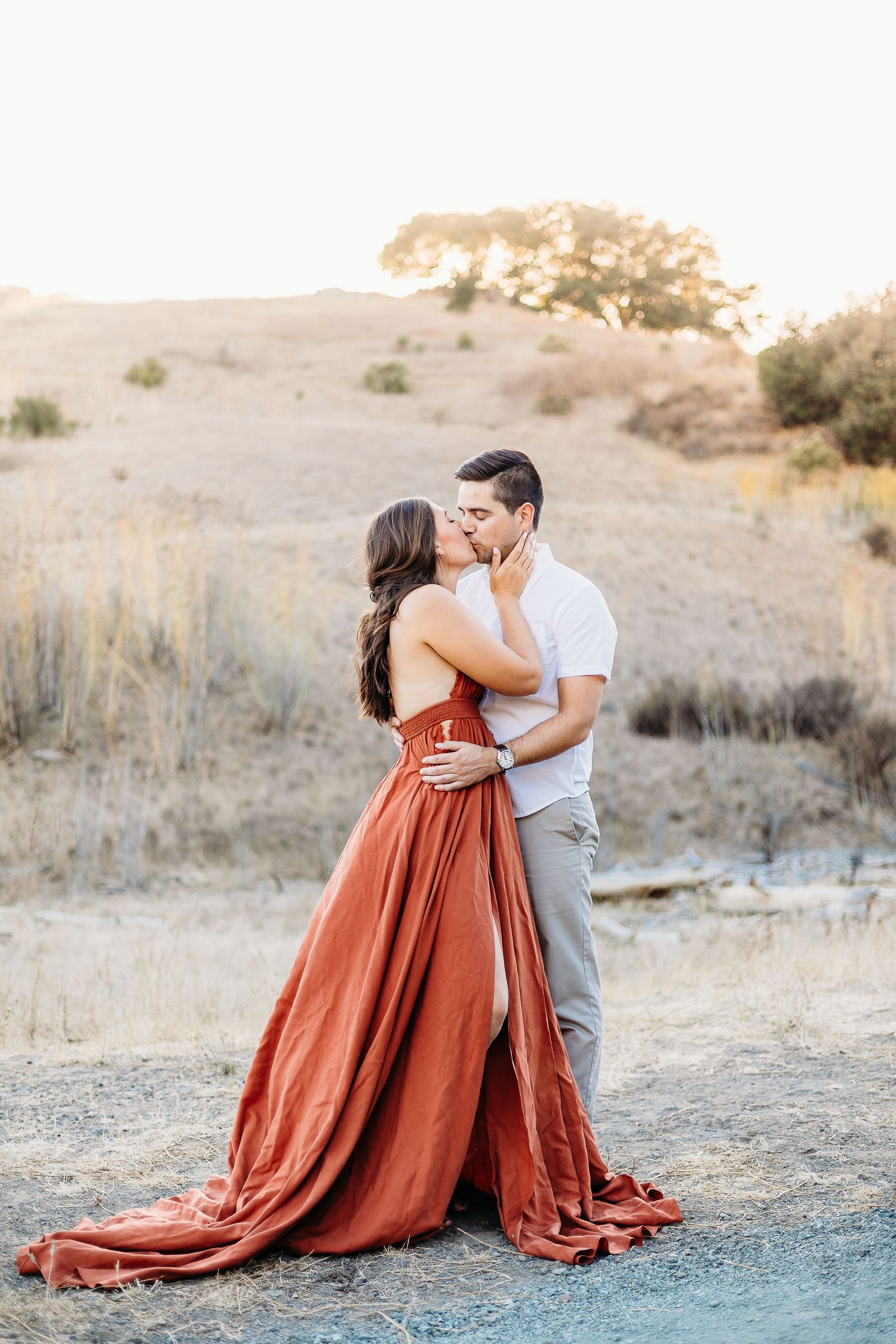 A romantic embrace captured at sunset with golden hills in the background.