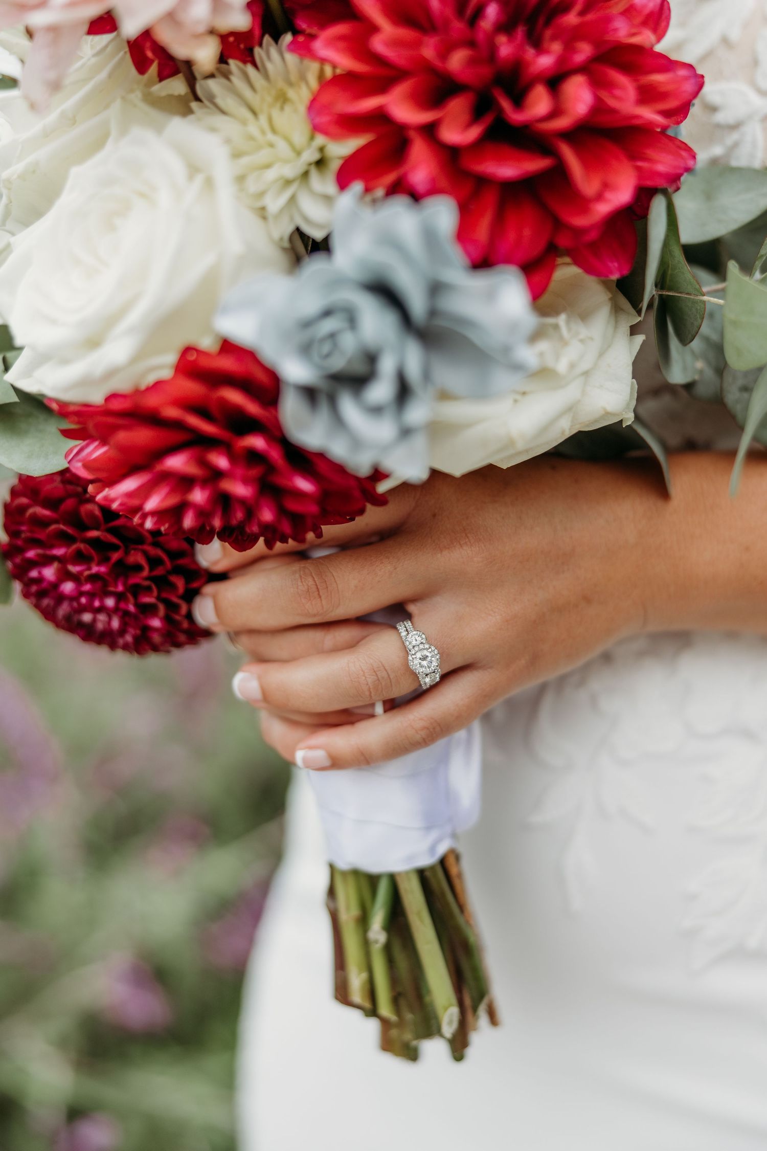 Close-up of red and white wedding bouquet with silver succulents and engagement ring.