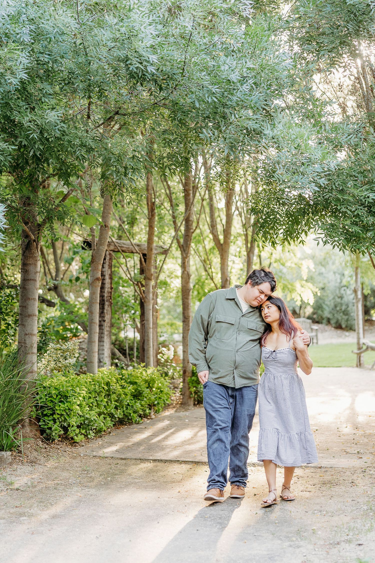 A romantic couple embraces on a tree-lined path during a golden hour photoshoot.