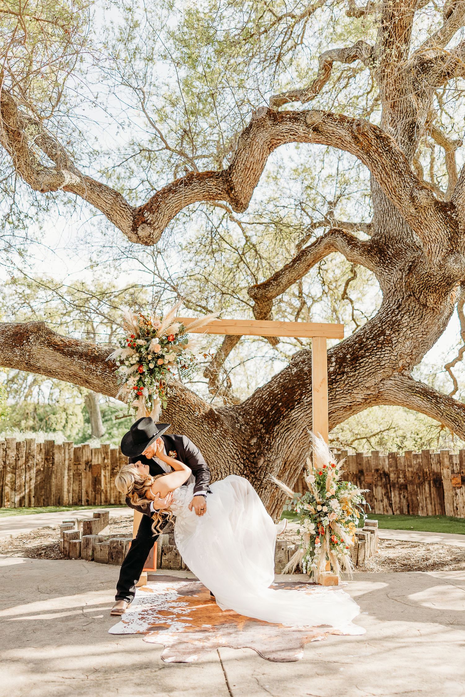 Beautiful outdoor wedding ceremony setup under a majestic twisted oak tree with wooden arch and floral decorations.