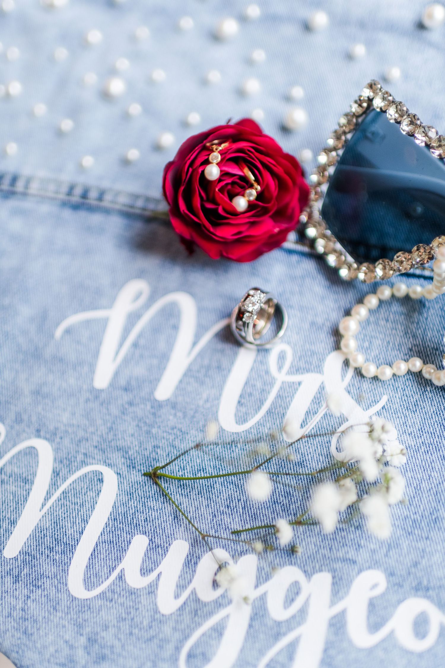 Wedding details with a red rose, pearl decorations, and text on denim fabric.