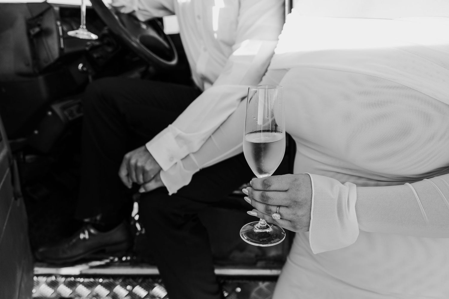 Multiple hands raising wine glasses in a black and white photograph at an outdoor gathering.