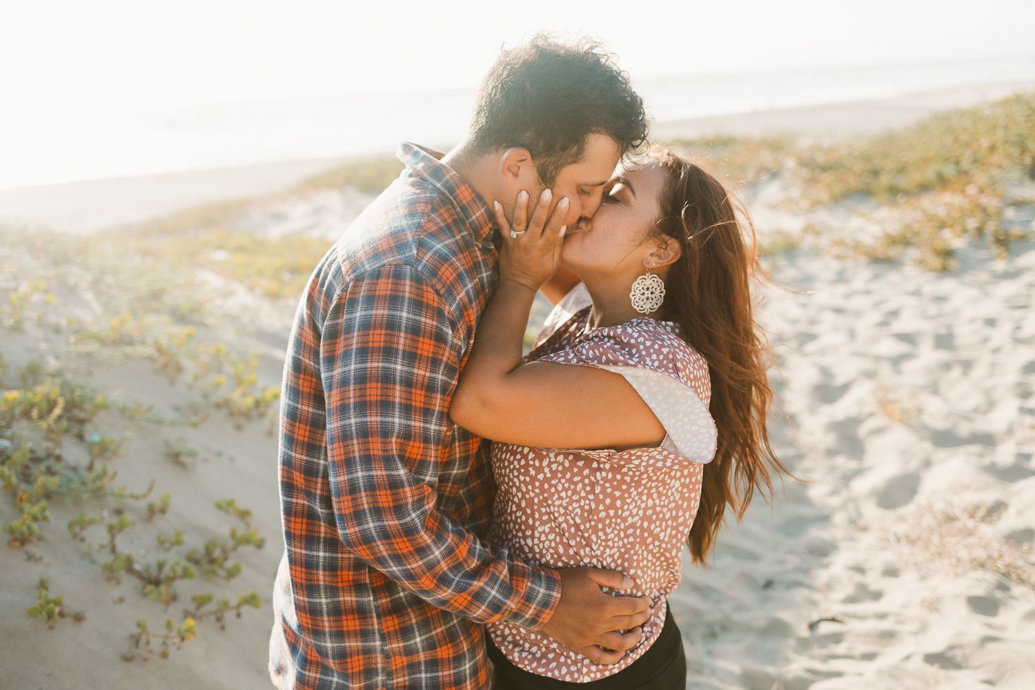 Romantic couple sharing a tender kiss on a sandy beach during sunset.