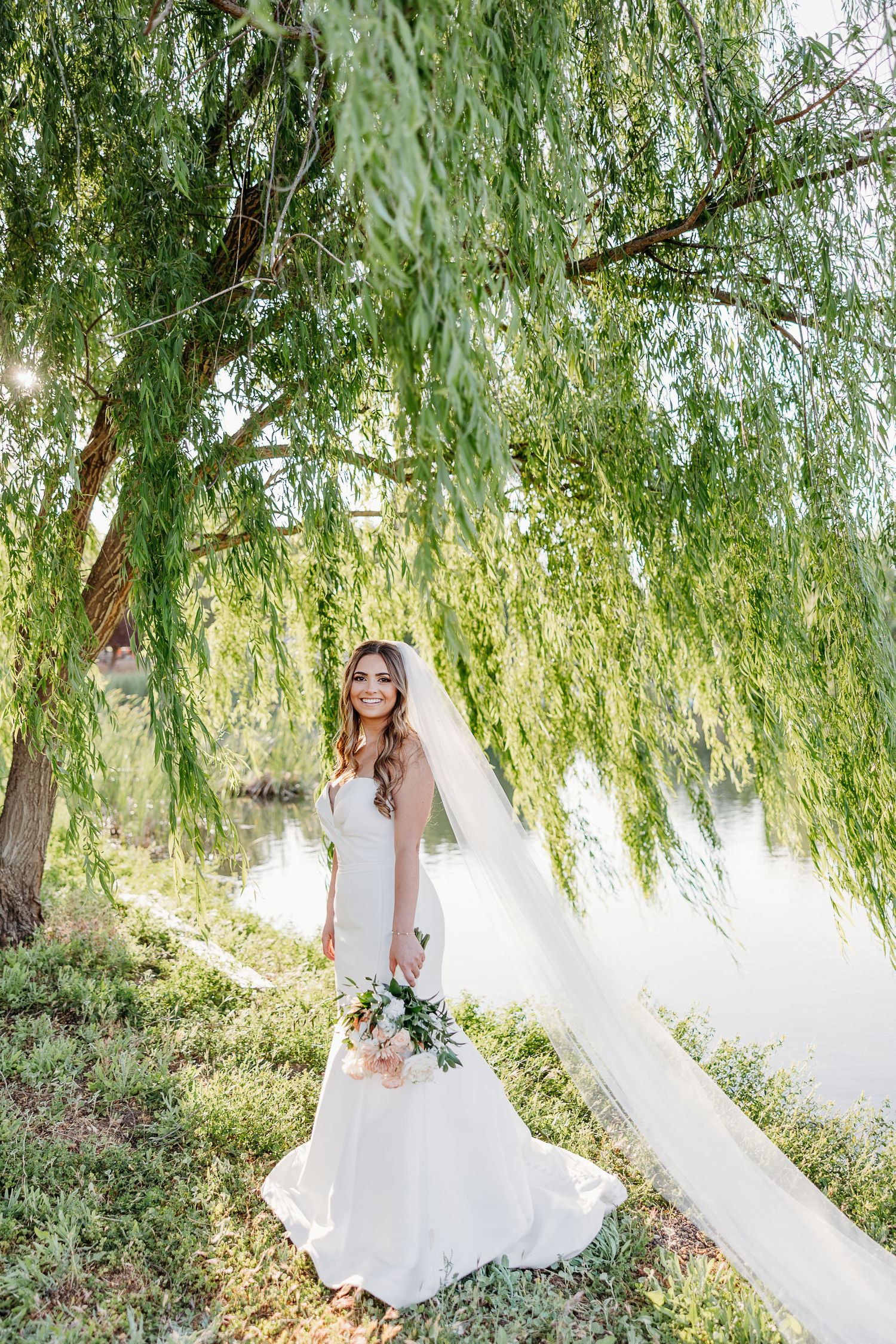 A serene bridal portrait under cascading willow tree branches in soft natural lighting.