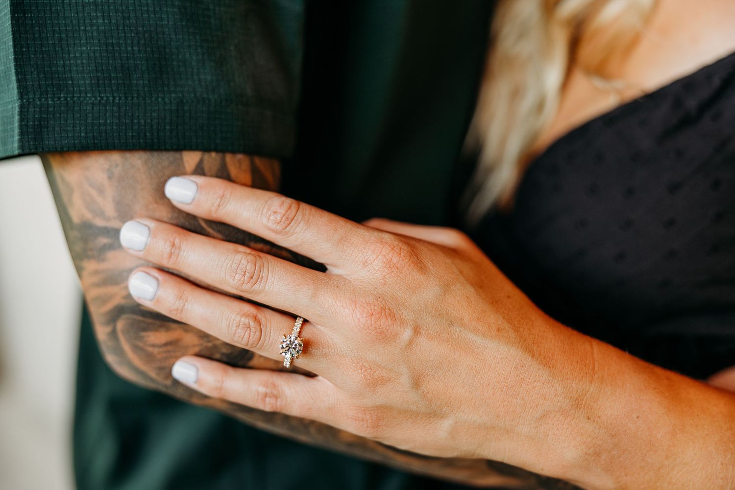 Close up shot of hands displaying engagement rings against a dark background.