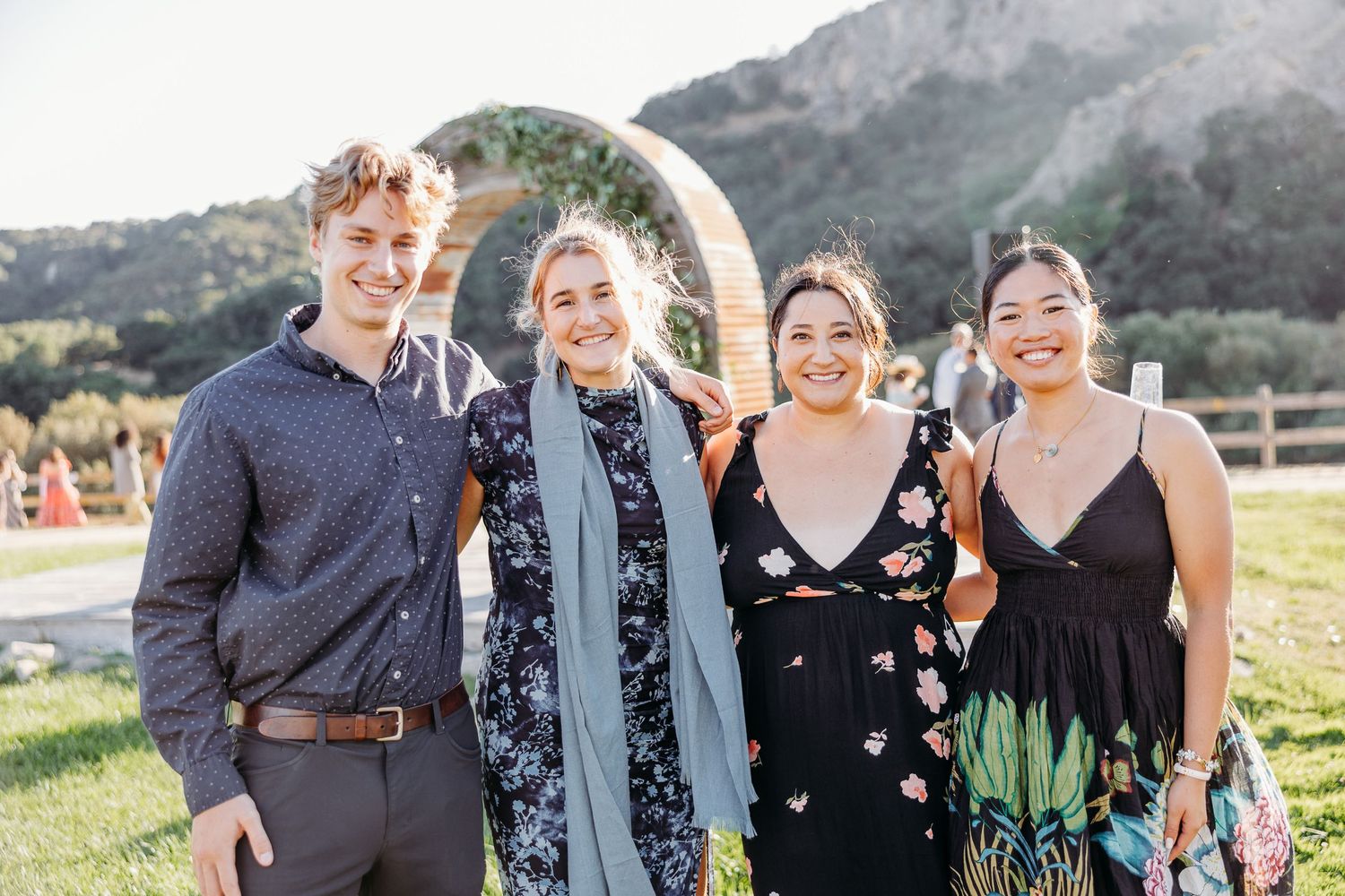 Group of people standing and smiling together outdoors with mountains visible in the background.