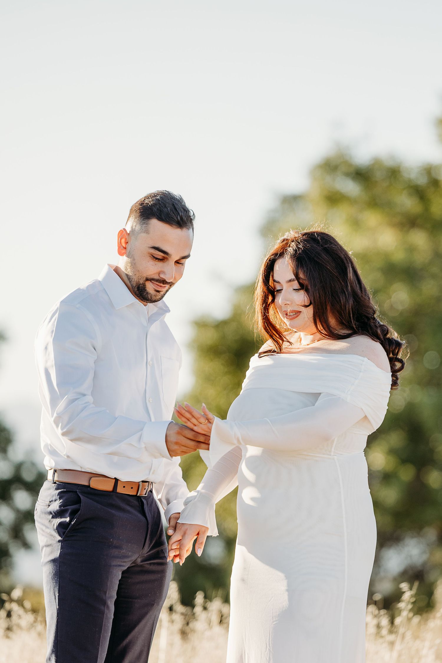 A couple in white and dark clothing share intimate moments while dancing together in a sunny outdoor setting.