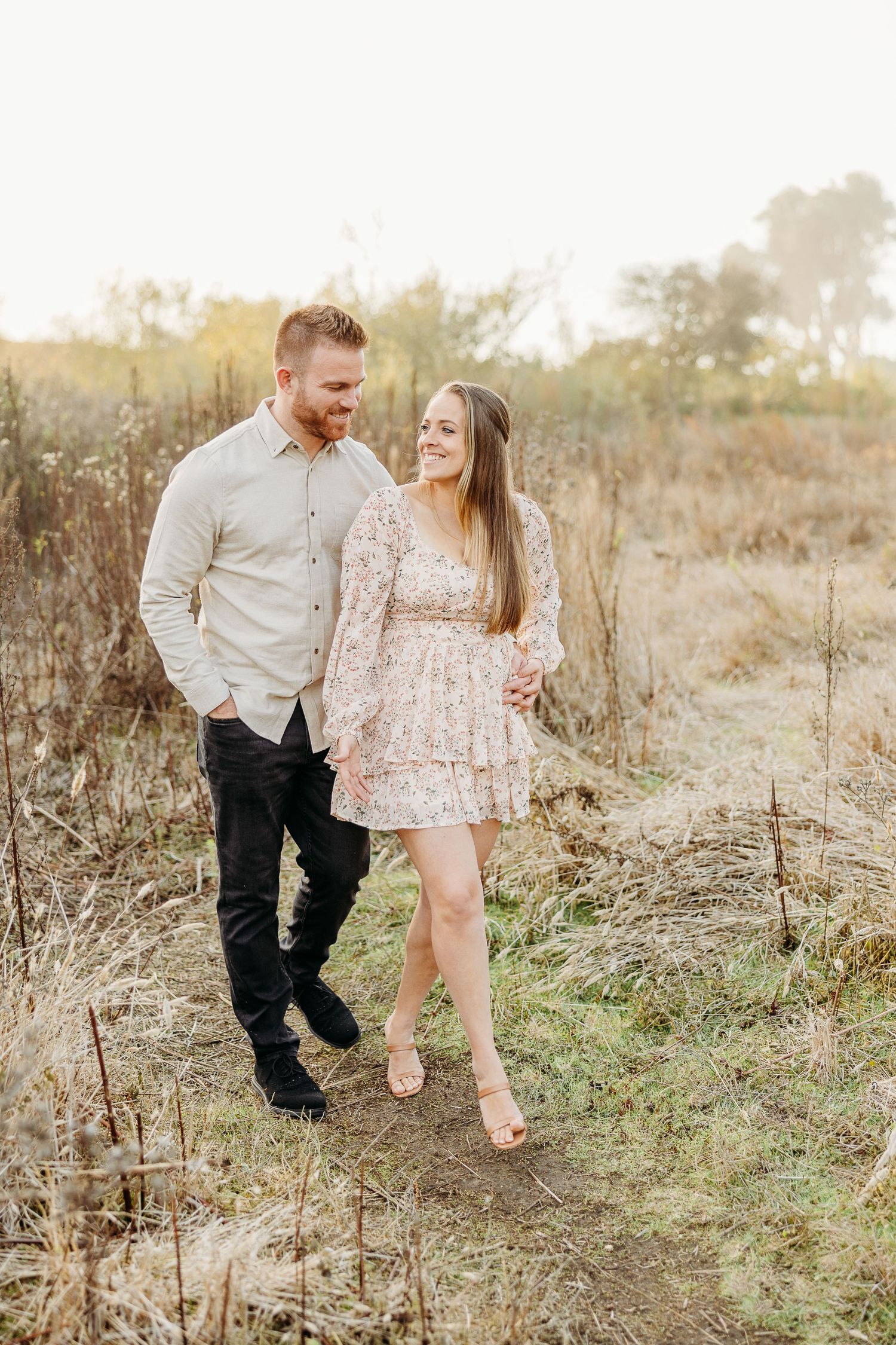 Couple takes a romantic stroll through tall grass during sunset in nature.
