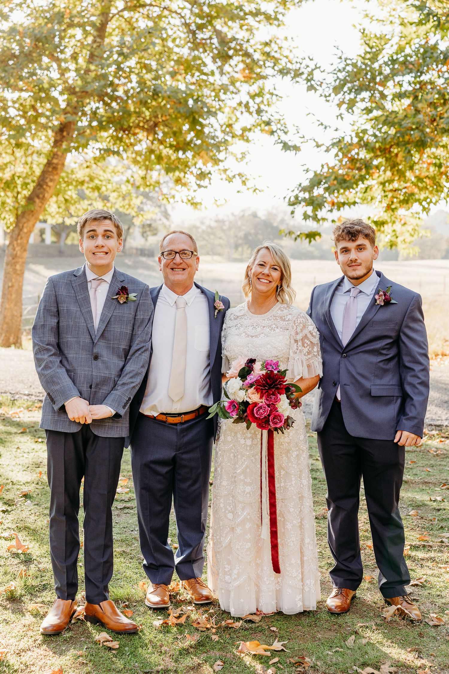 Wedding party in formal attire poses together under autumn trees.