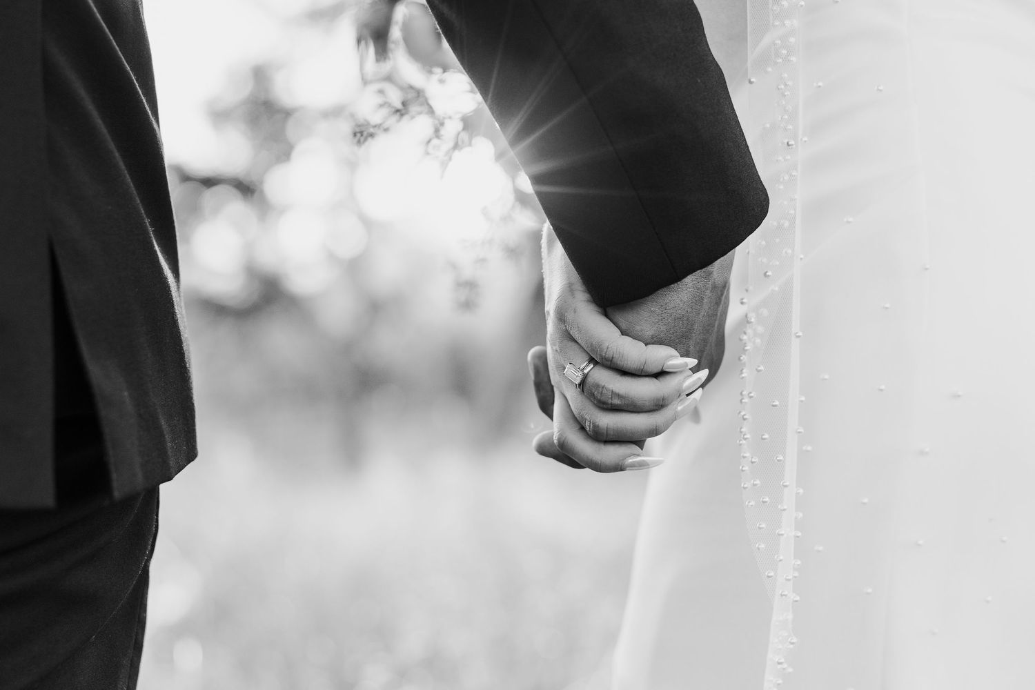 Black and white detail shot of couple holding hands during wedding ceremony.