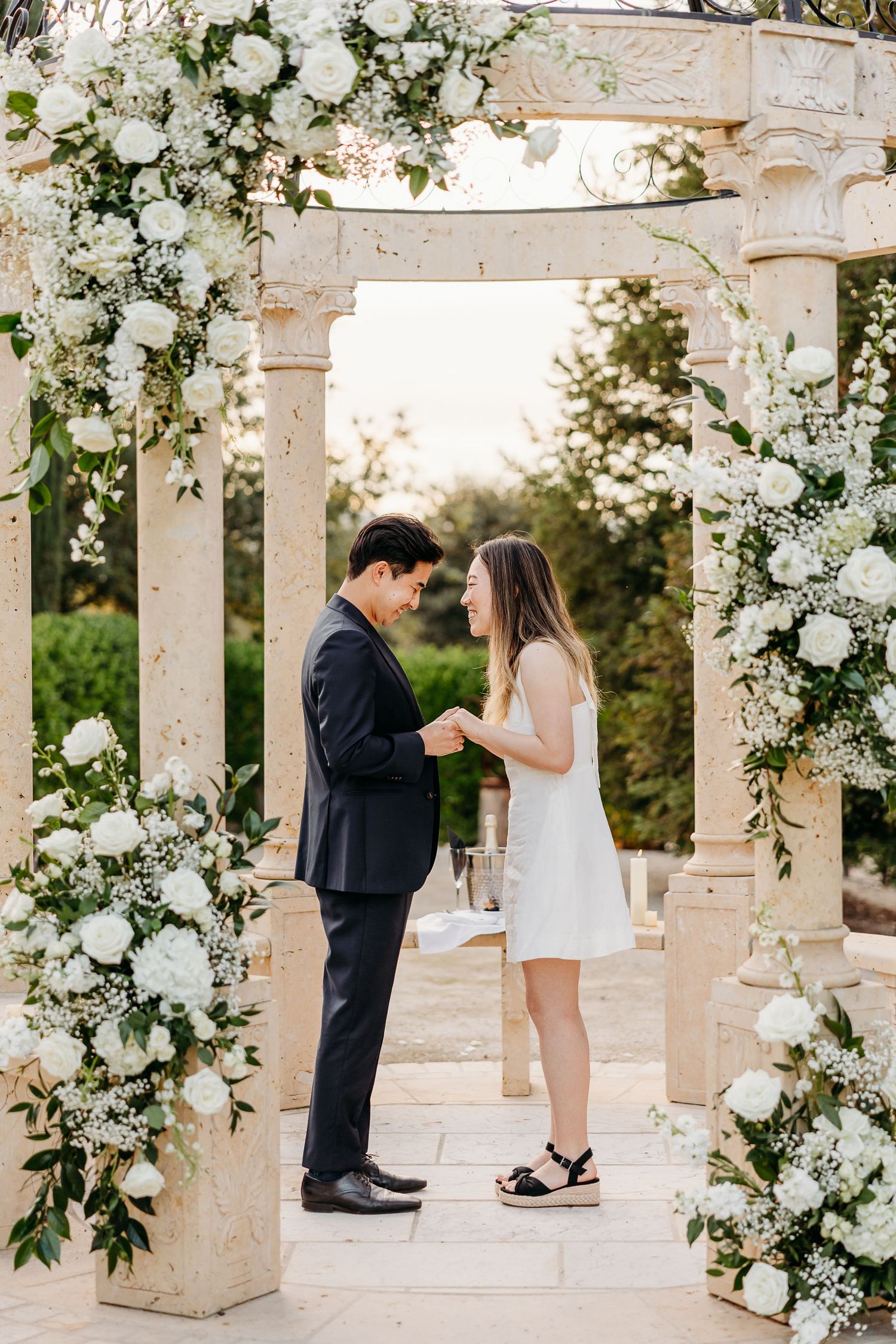 An elegant stone gazebo in Paso Robles adorned with white roses and greenery creates a romantic outdoor setting.