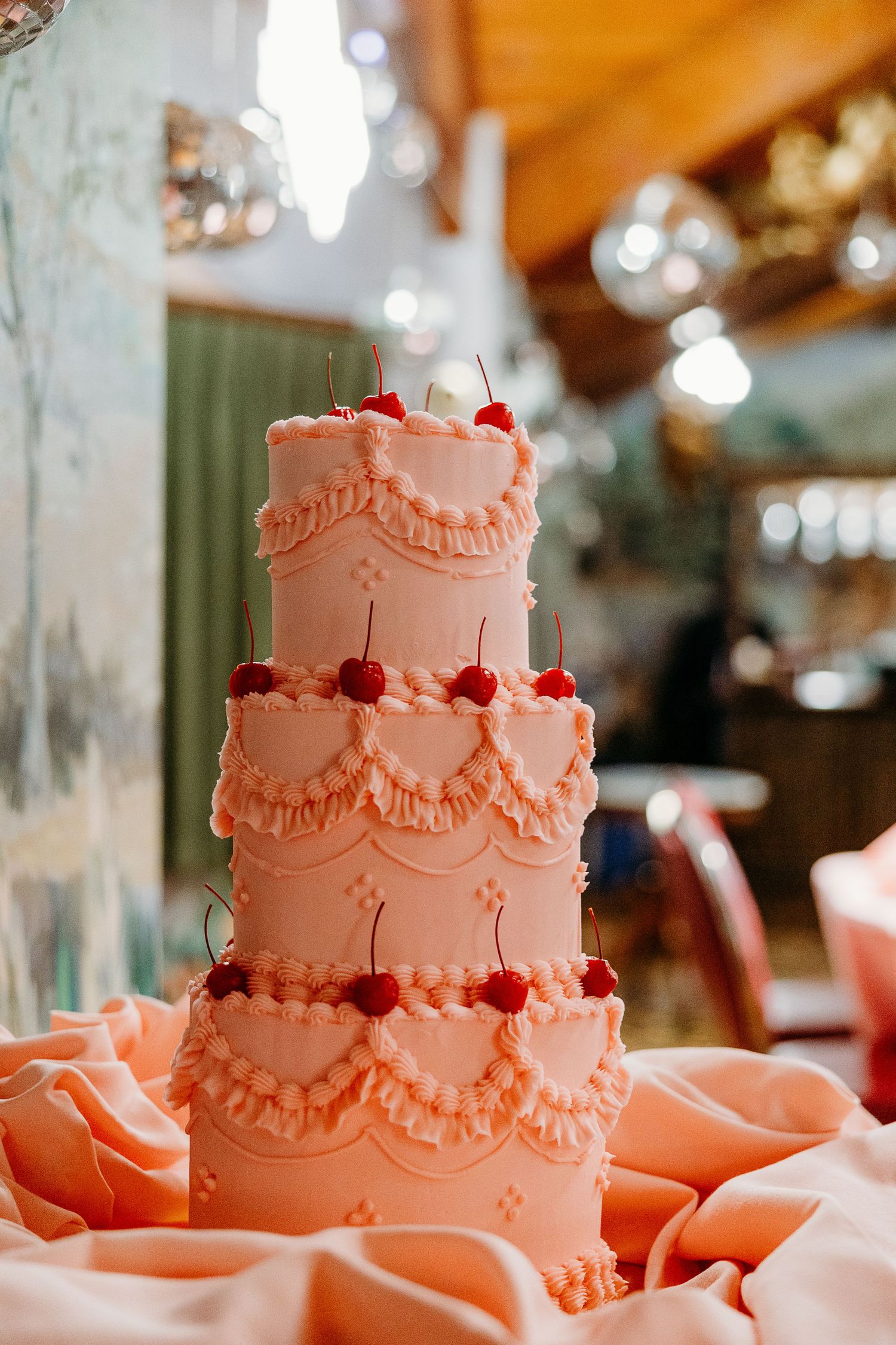 A three-tiered coral wedding cake with delicate piped details and red accents.