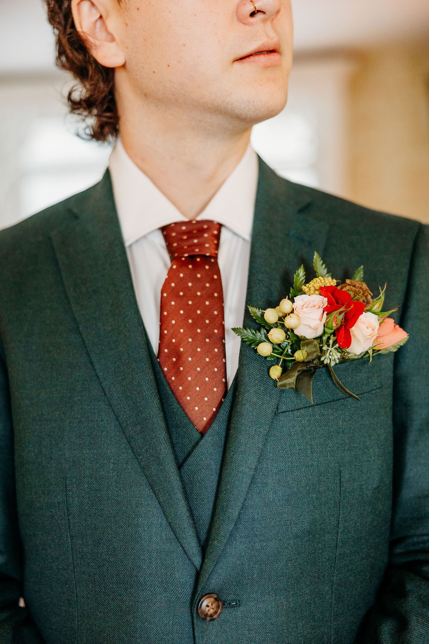 Close-up view of a dark green suit jacket with polka dot burgundy tie and coral boutonniere.