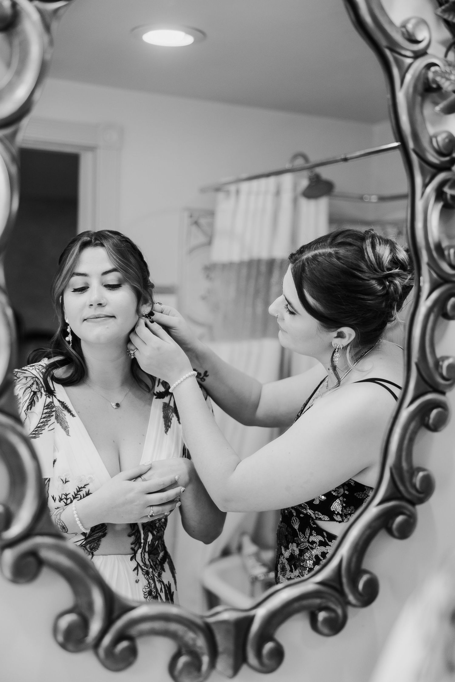 Black and white image showing wedding preparation with ornate mirror reflections and makeup application.