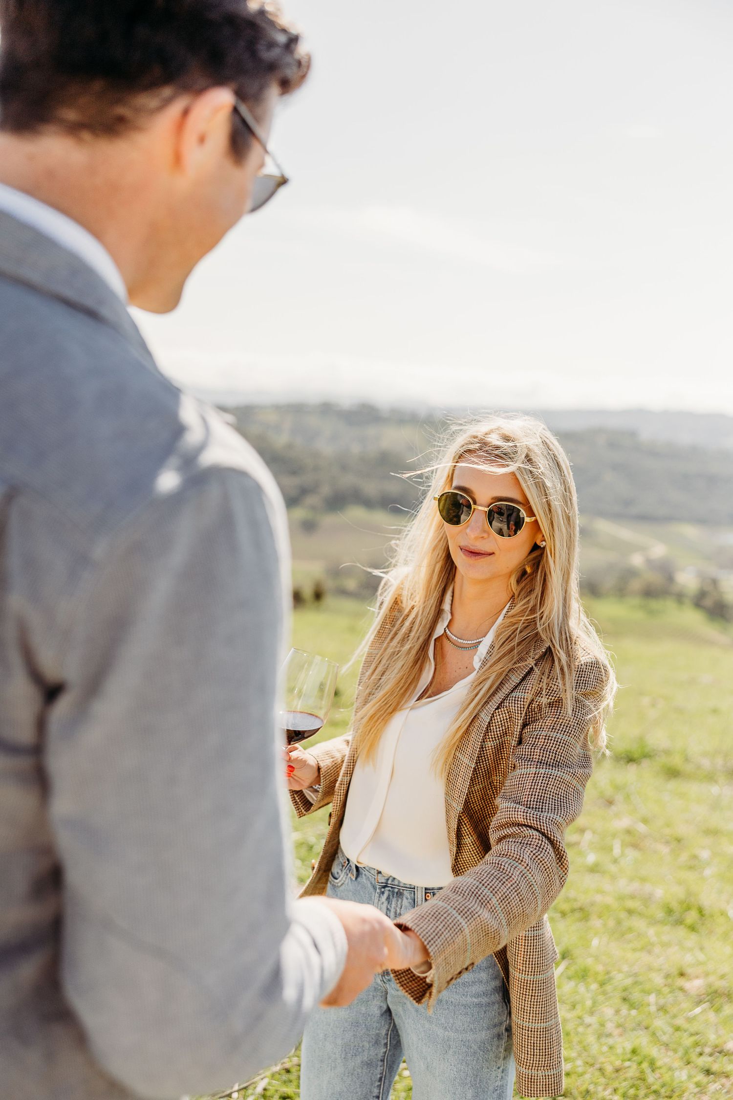 Couple enjoying wine and conversation in a scenic hillside setting.
